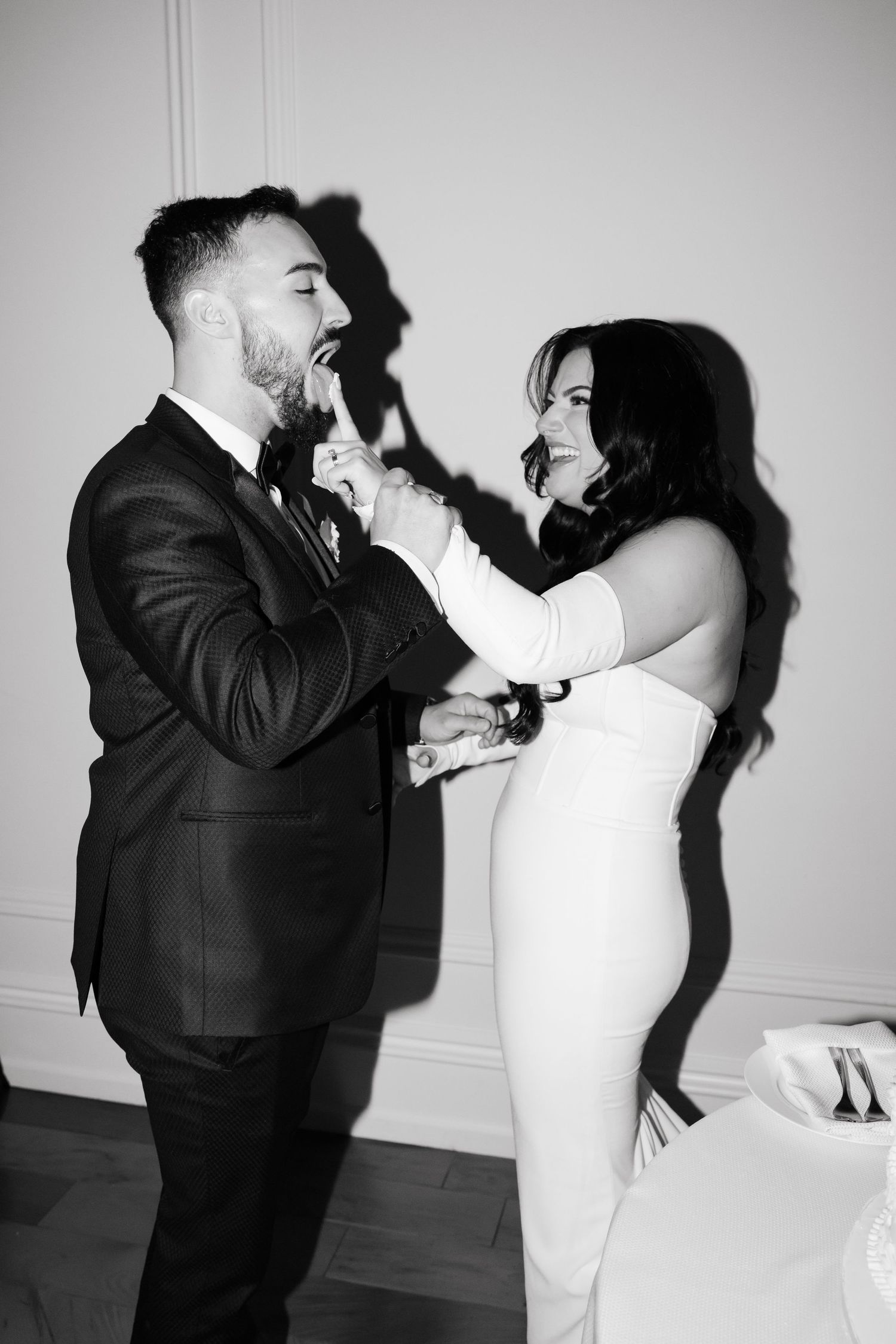 Black and white capture of joyful couple sharing cake at their wedding celebration.
