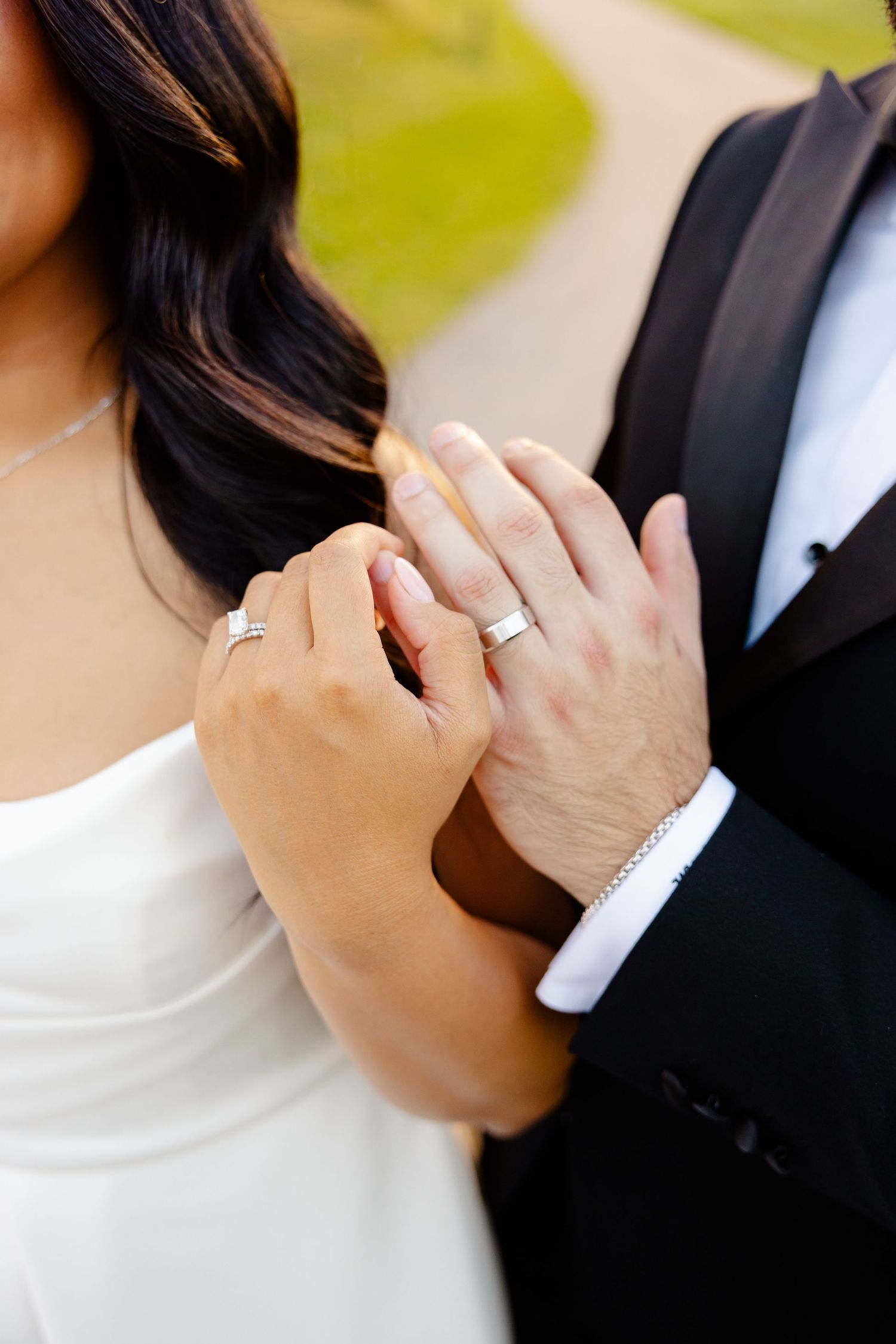 Close-up of bride and groom's hands showing their wedding rings against white dress and black suit.