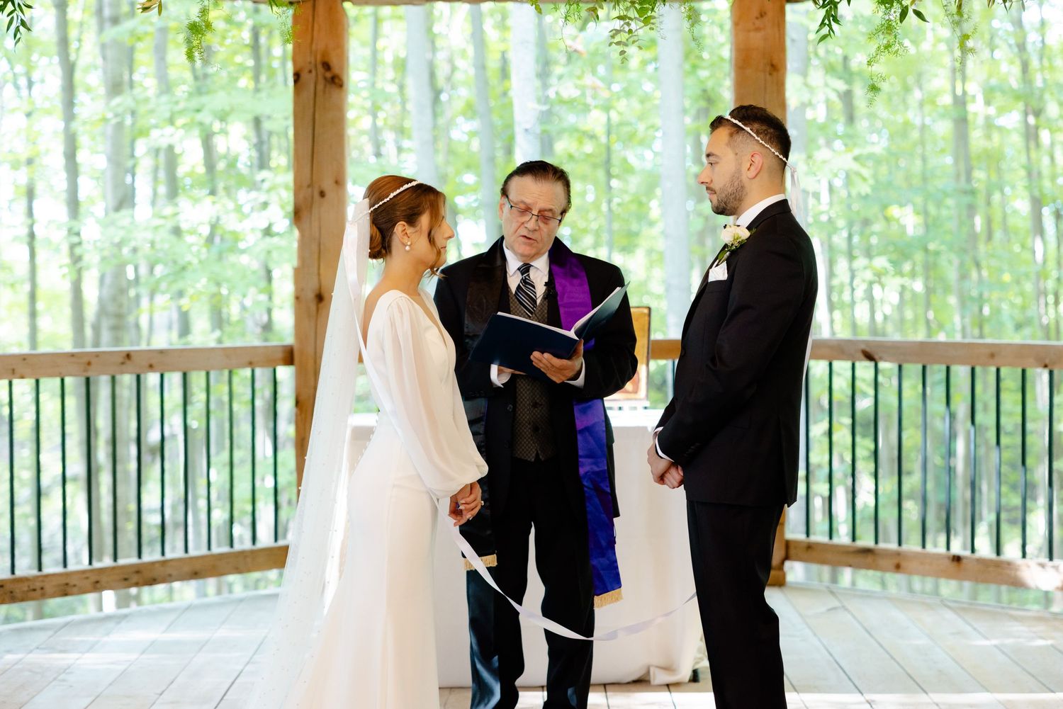 Intimate wedding ceremony under wooden beams with natural forest backdrop.