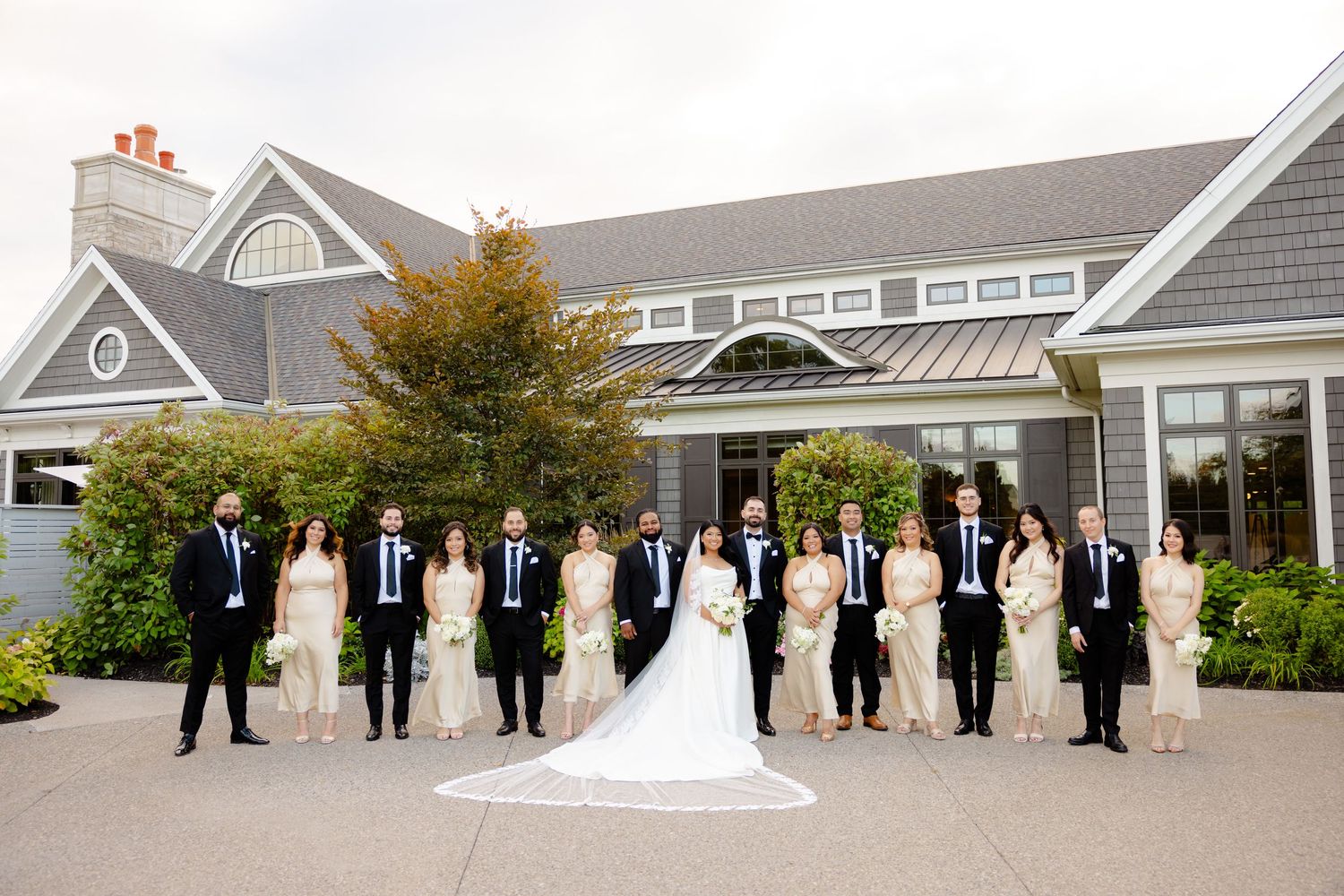 Wedding group stands in line formation outside elegant gray building with autumn accents.