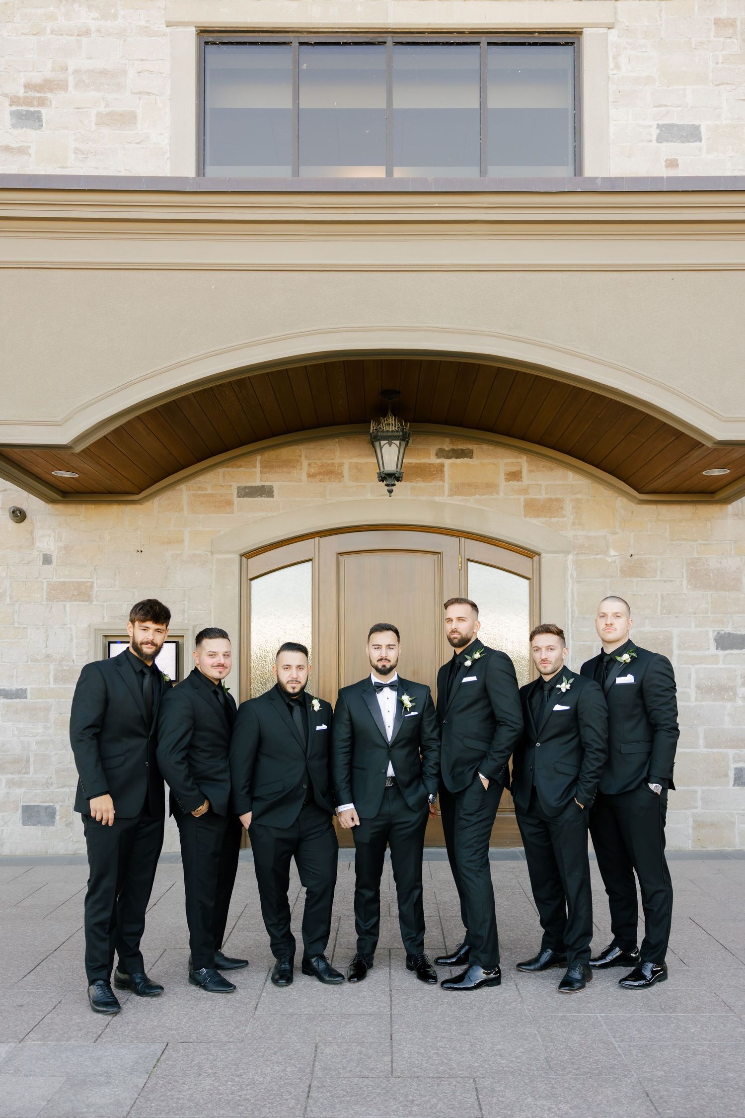 Groomsmen lined up for a formal photo against stone architecture with an arched doorway.