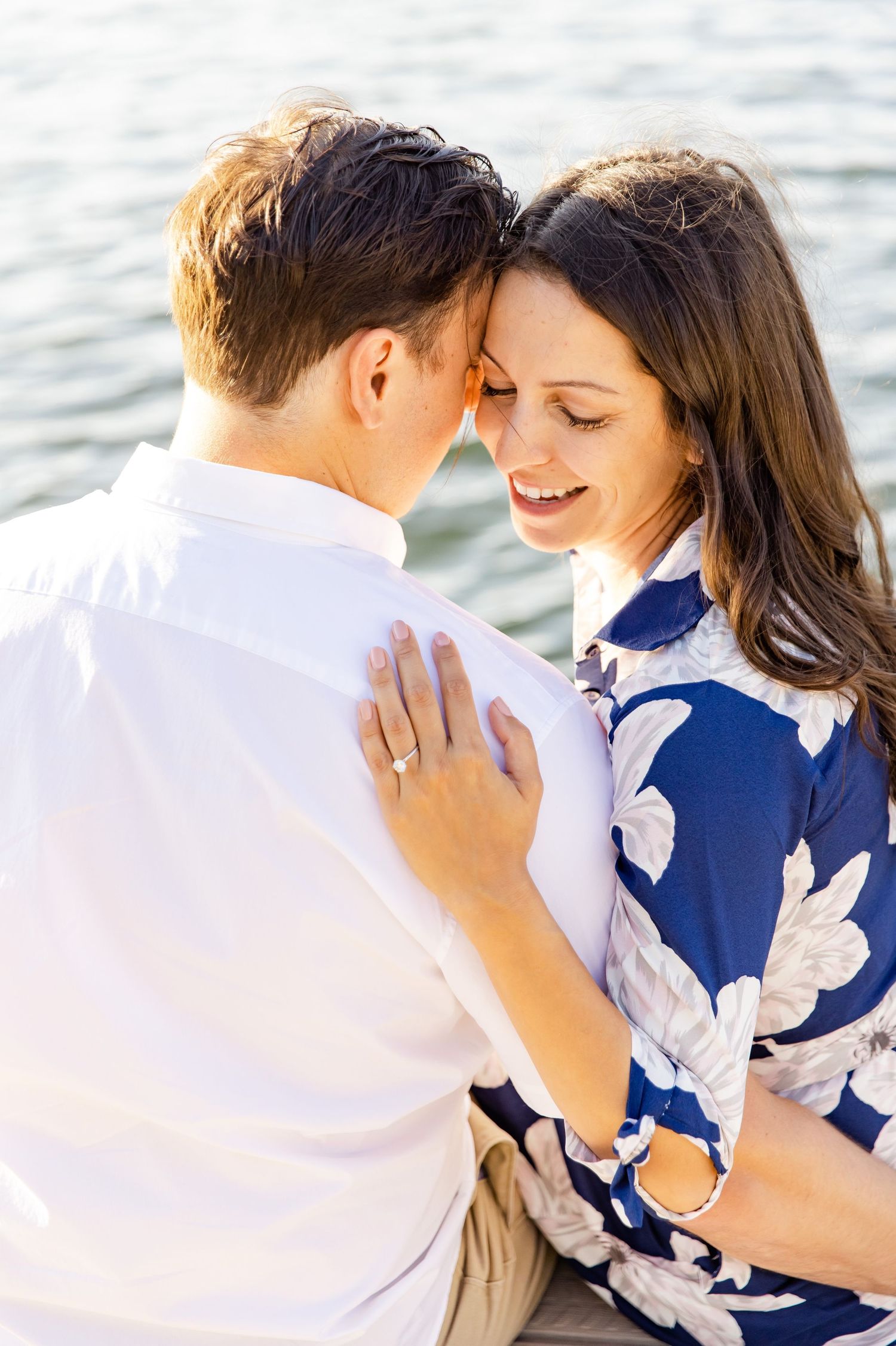 Intimate moment between couple in coordinated outfits on lakeside dock during sunset.