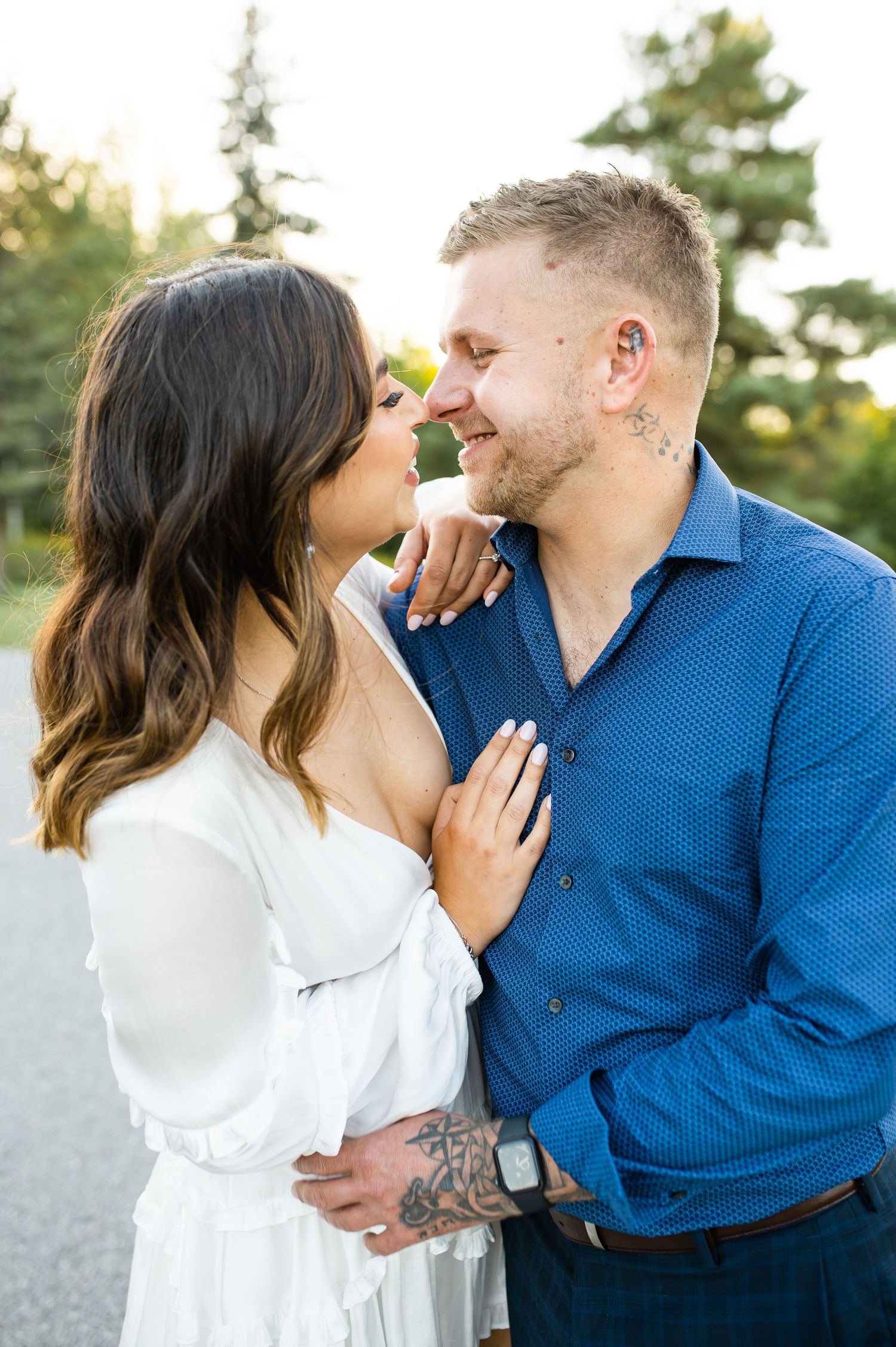 Intimate couple portrait outdoors with sunlit trees in background.