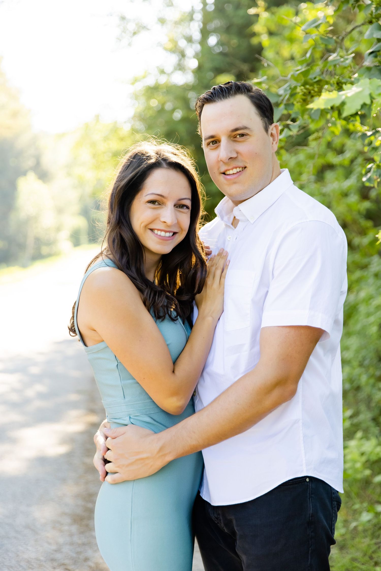 Couple in white and blue outfits posing together on a sunny outdoor path.