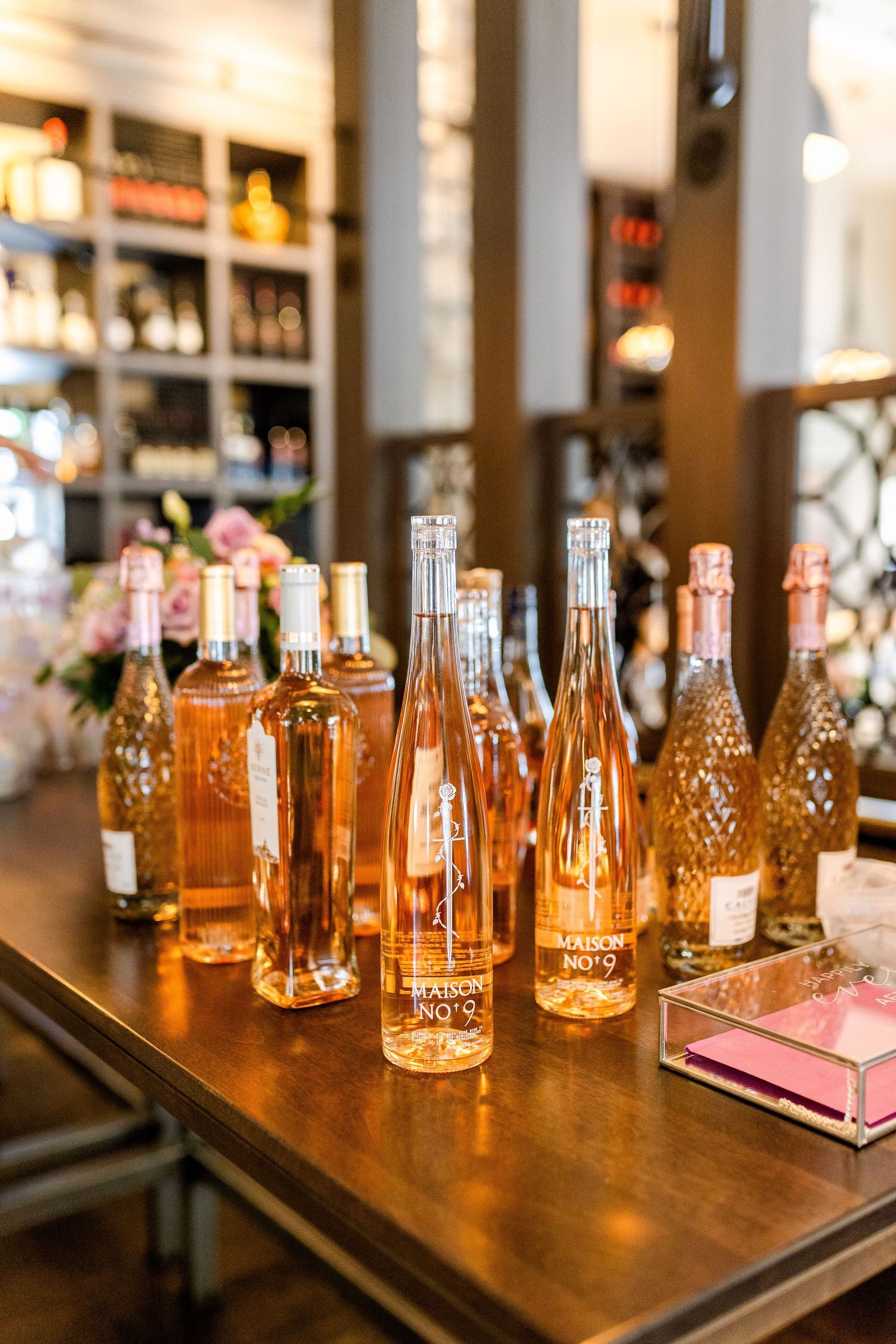 Multiple bottles of rose wine displayed on a wooden table with floral decorations in the background.