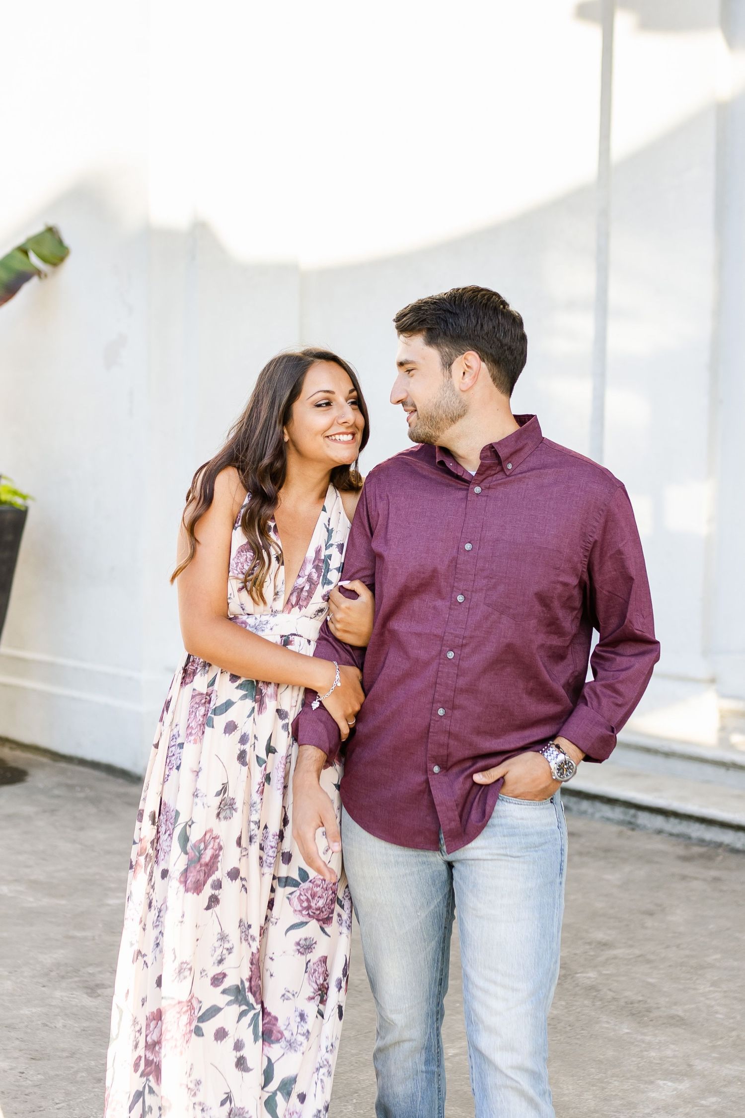 A romantic moment between couple wearing floral dress and burgundy shirt near white columns.