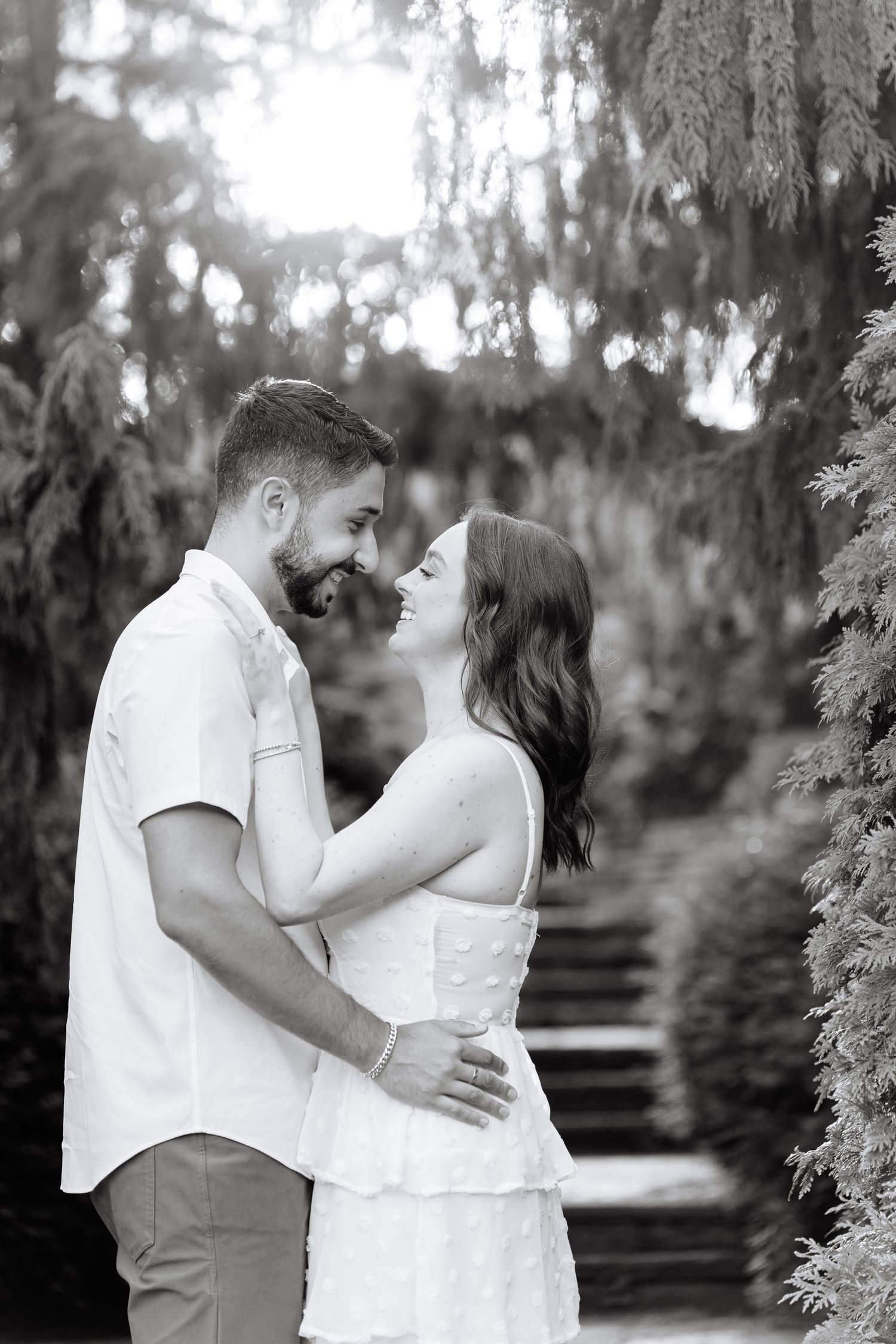 Black and white portrait of a couple sharing an intimate moment in a garden setting.
