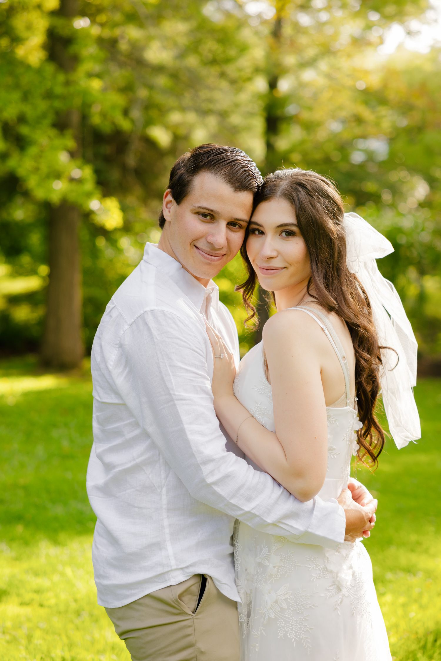 Wedding couple embraces in a sunny garden setting wearing white and khaki casual wedding attire.