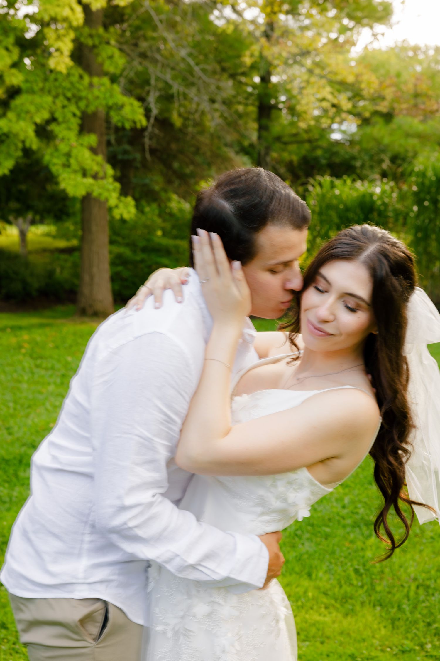 A couple in wedding attire embracing while sharing an intimate moment outdoors.