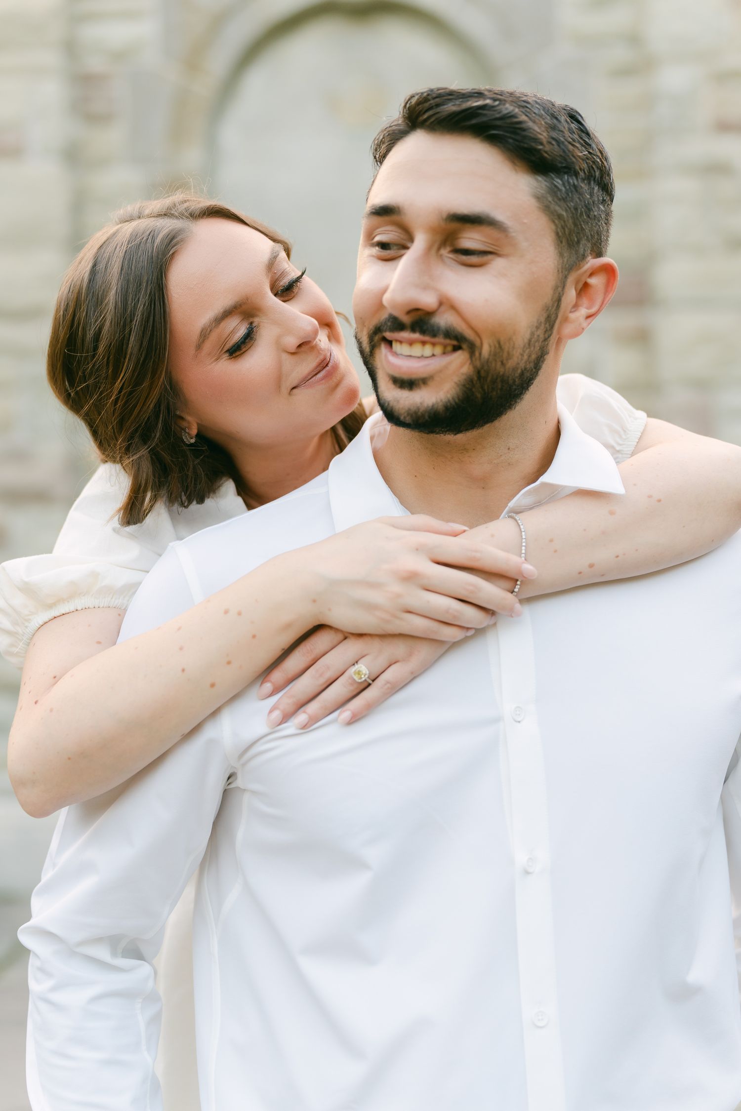 A tender moment captured between a couple in white outfits against a stone wall backdrop.