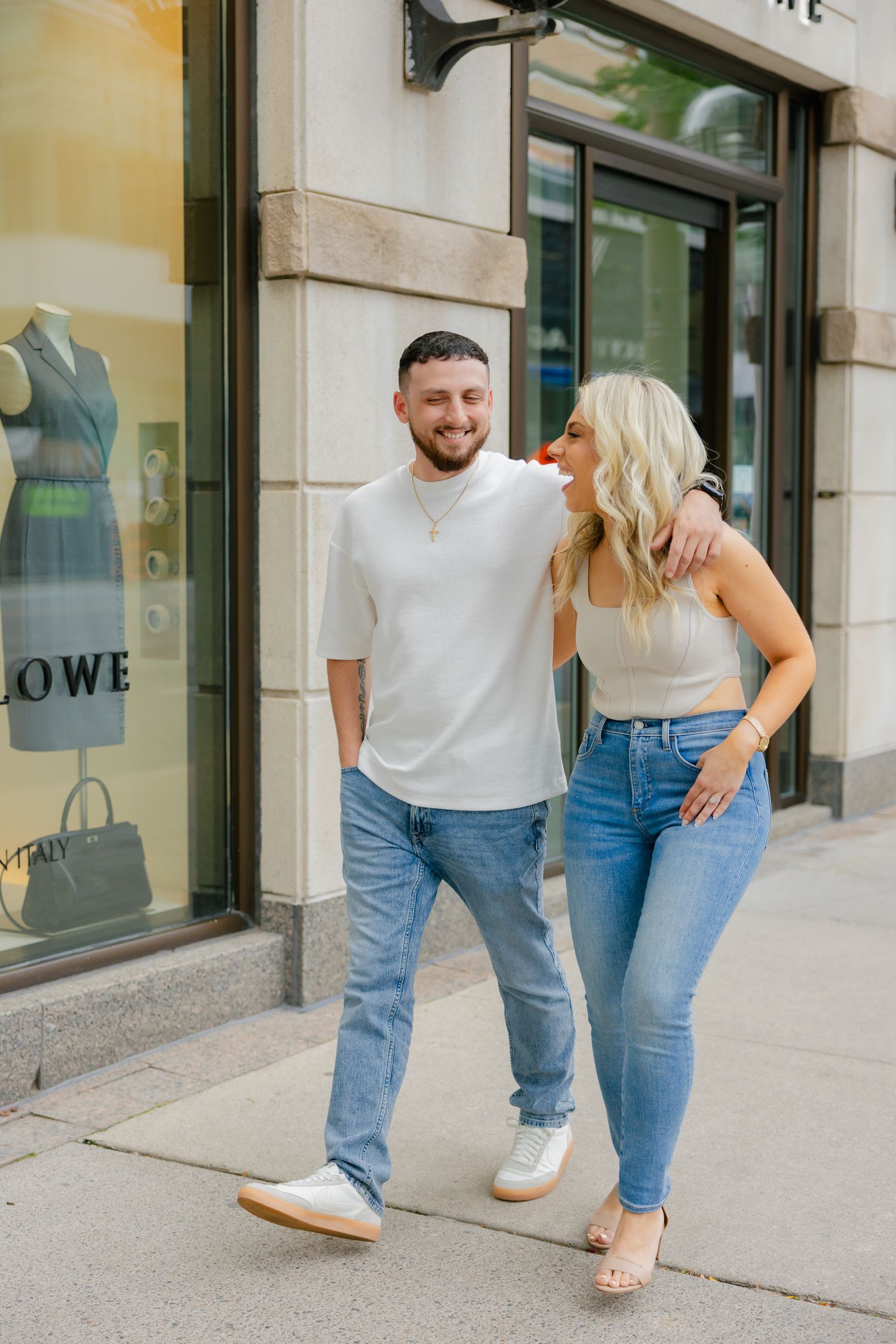 Casual couple laughing together outside storefront in coordinated outfits.