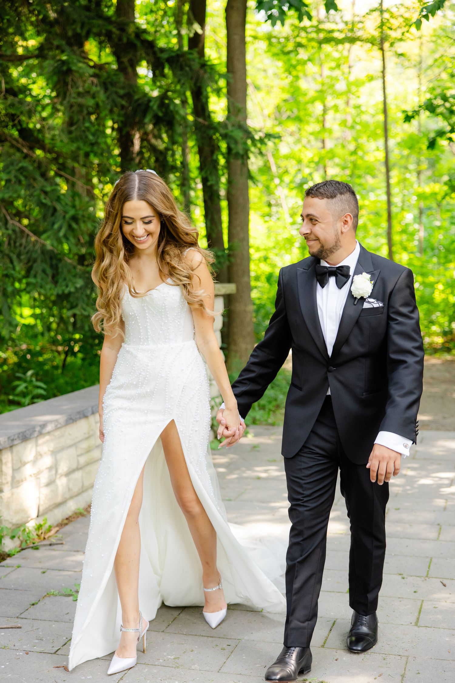 Wedding couple sharing a romantic walk on stone pathway through vibrant forest setting.