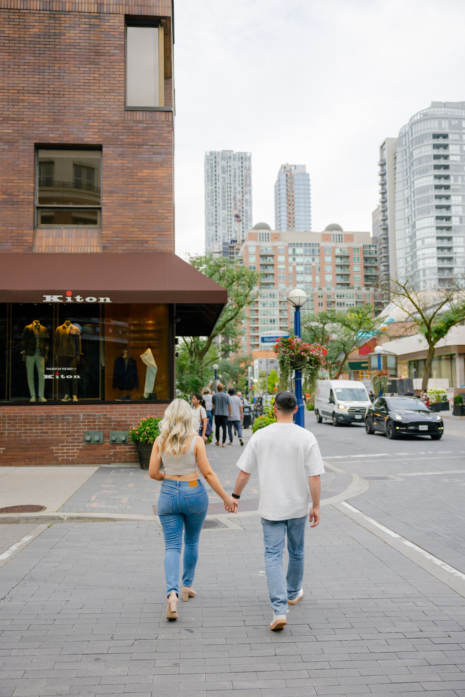 Couple walking together on brick pavement near modern city buildings and shops.