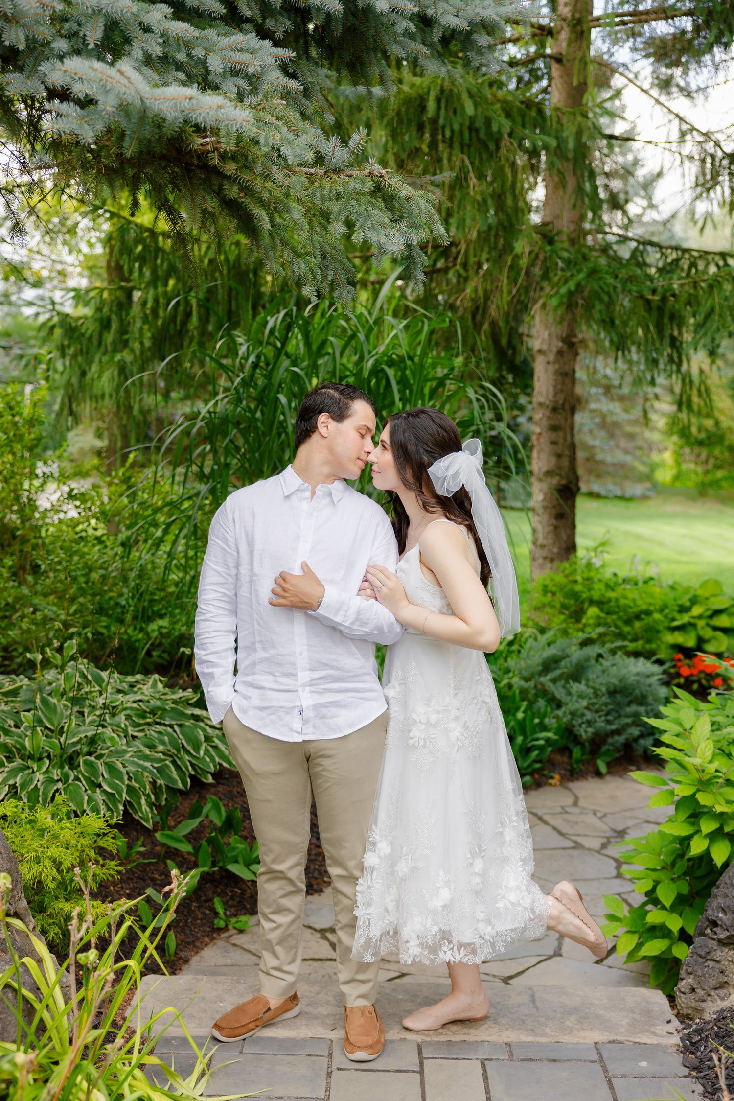 Wedding couple stands together on stone path surrounded by lush garden landscaping.
