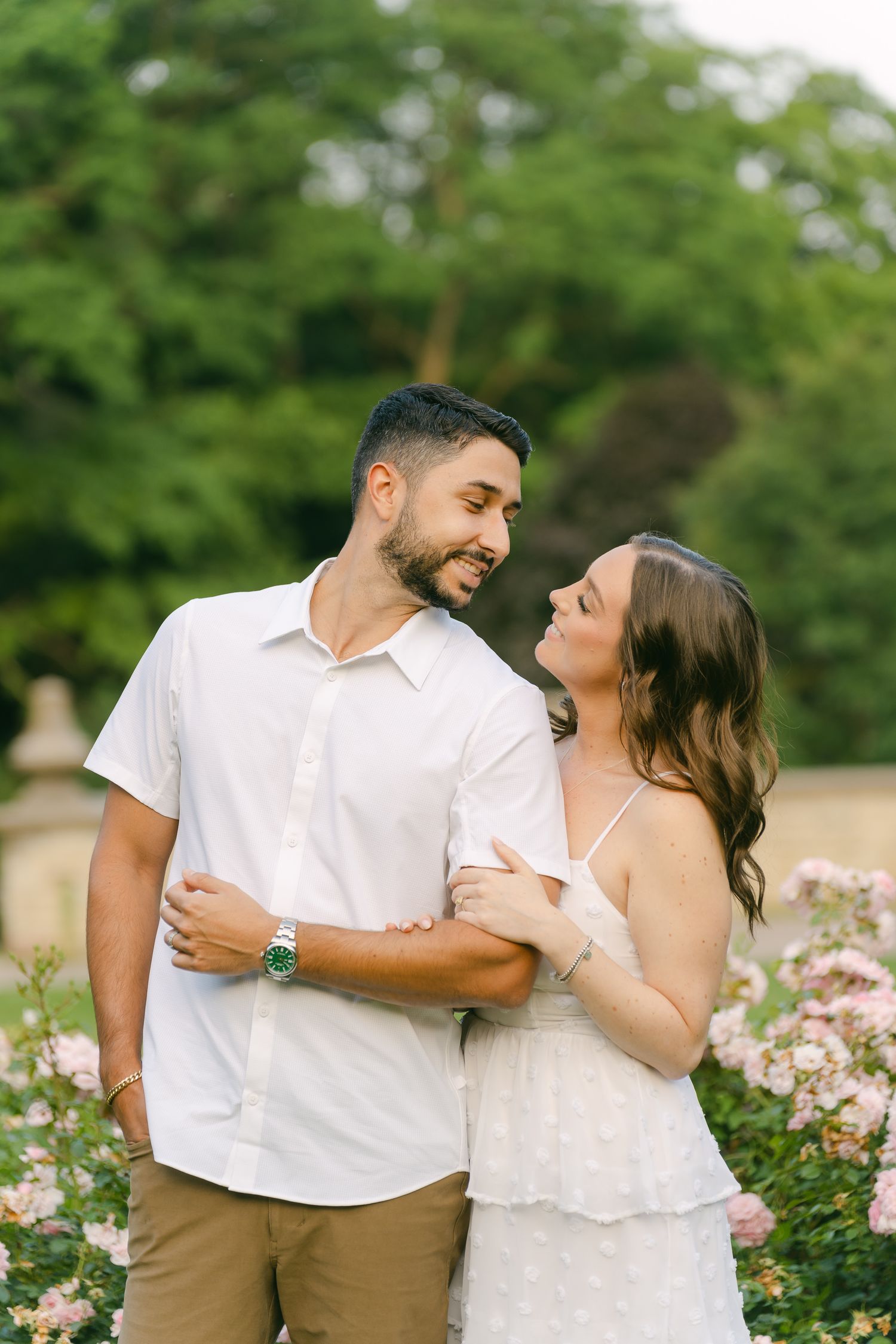 A romantic couple shares a tender moment while standing in a garden with blooming pink flowers.