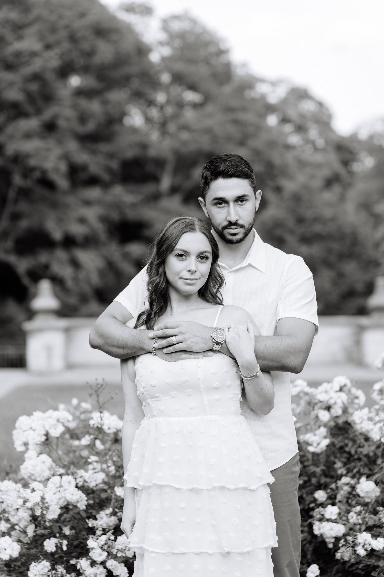 A black and white engagement photo showing a couple in an elegant garden setting.
