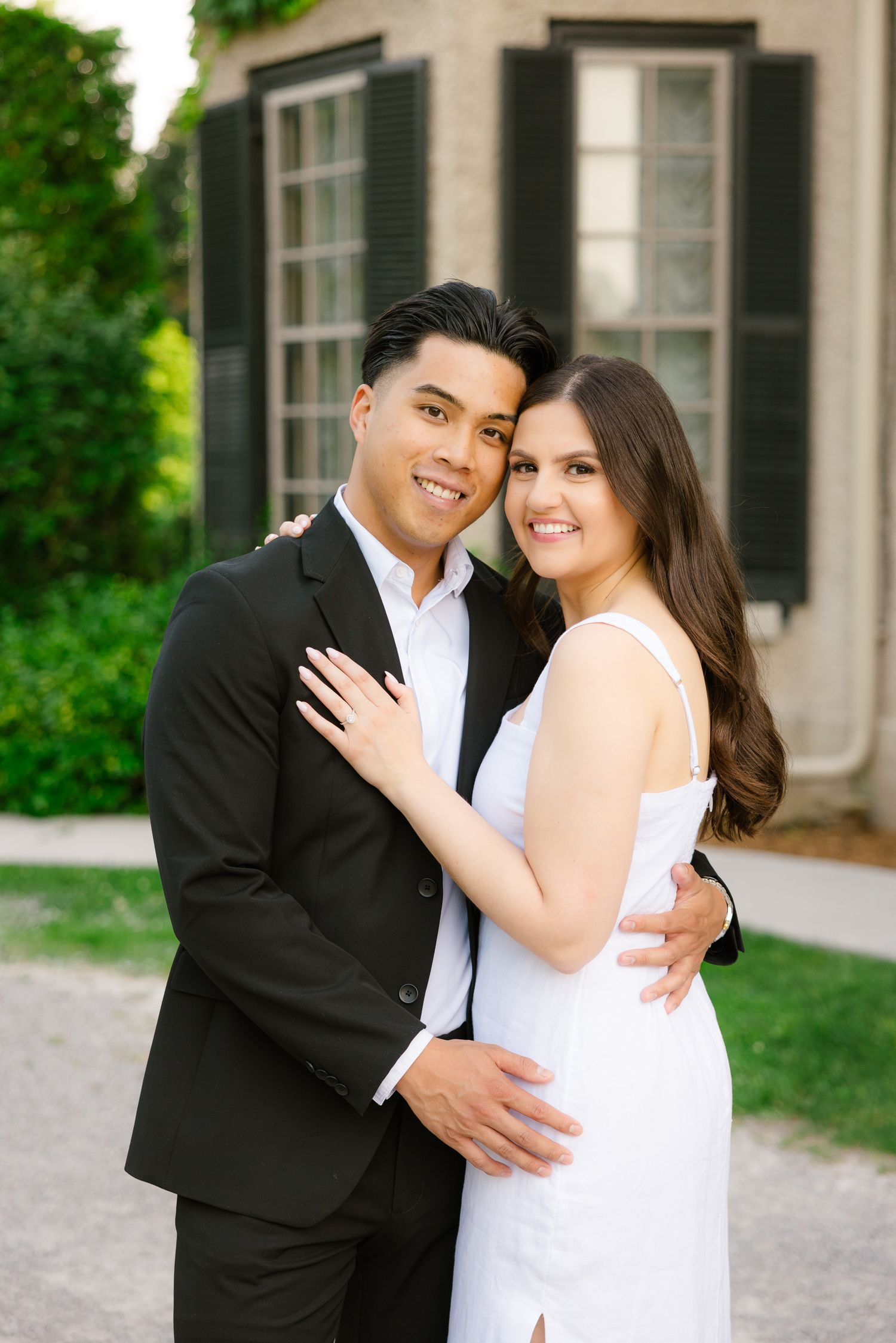 Happy couple in formal attire embracing outside historic mansion with ivy.