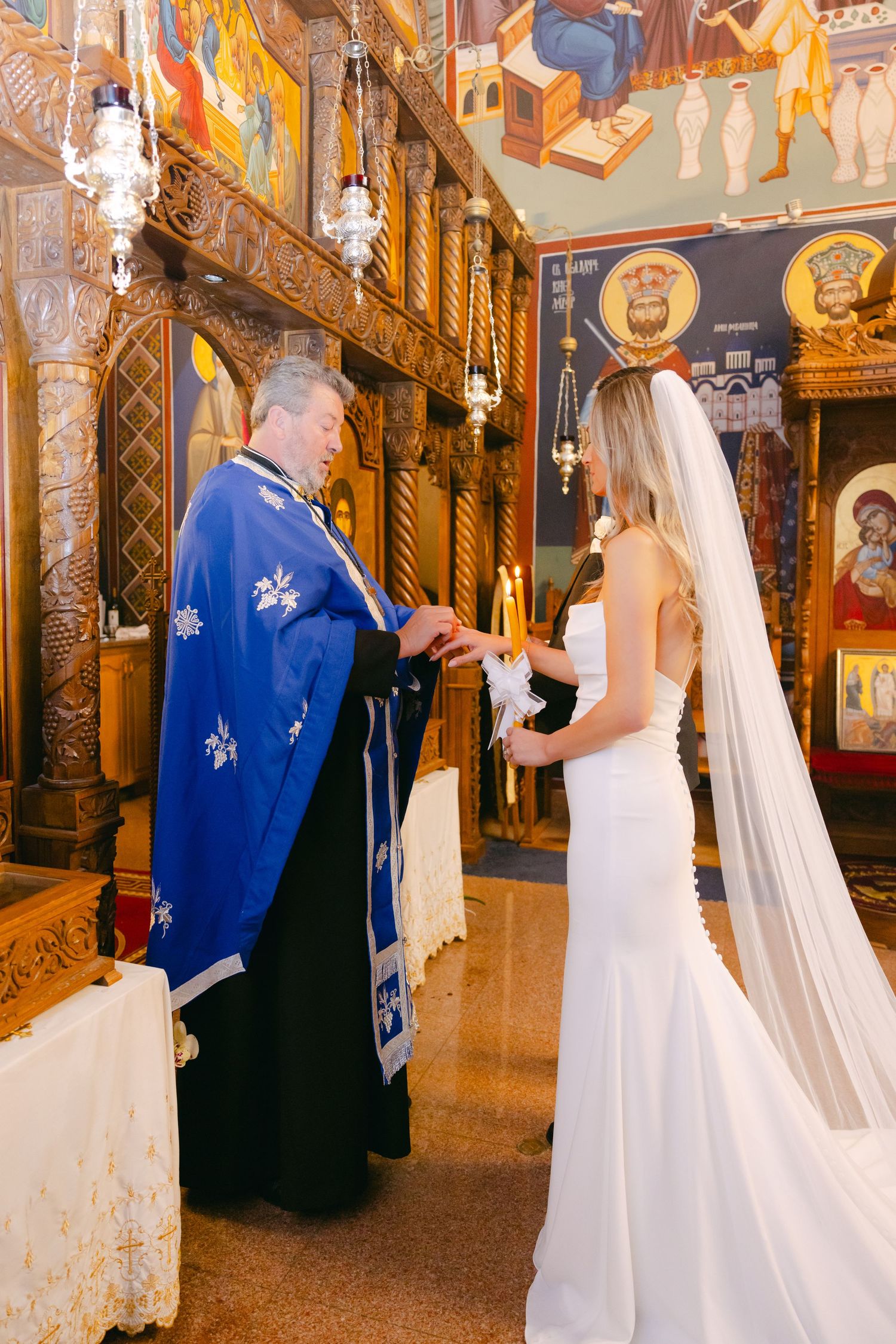 Orthodox wedding ceremony with priest and bride exchanging ritual items beneath ornate church decorations.