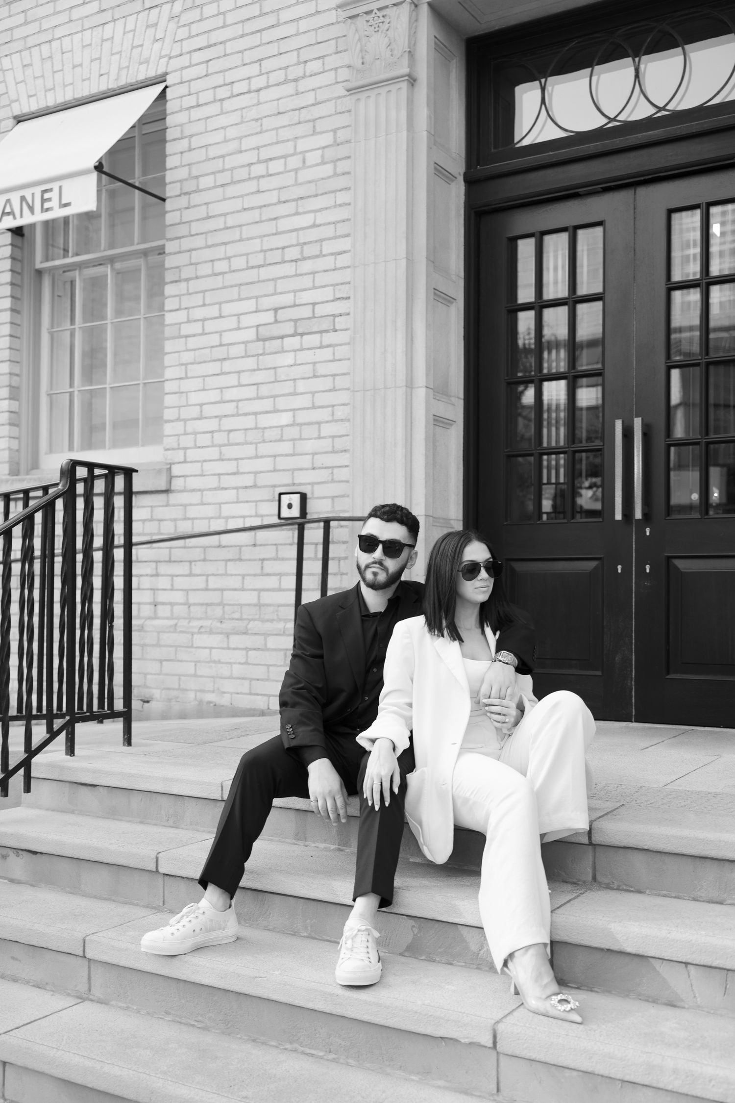 Black and white photo of couple relaxing on stone steps outside luxury retail store.