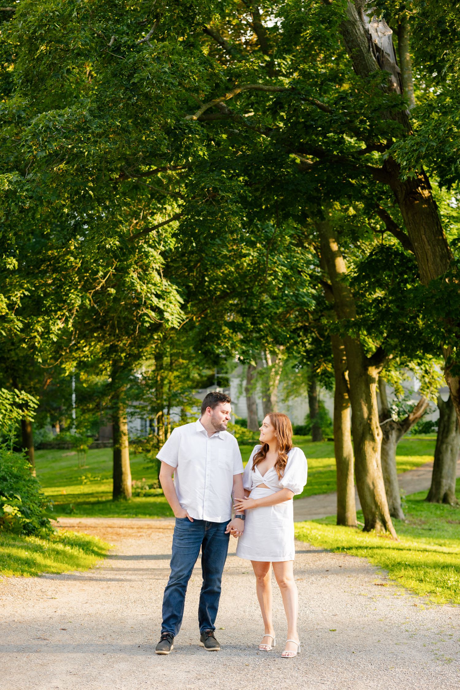A couple walks together on a tree-lined path in a park during a sunny afternoon.