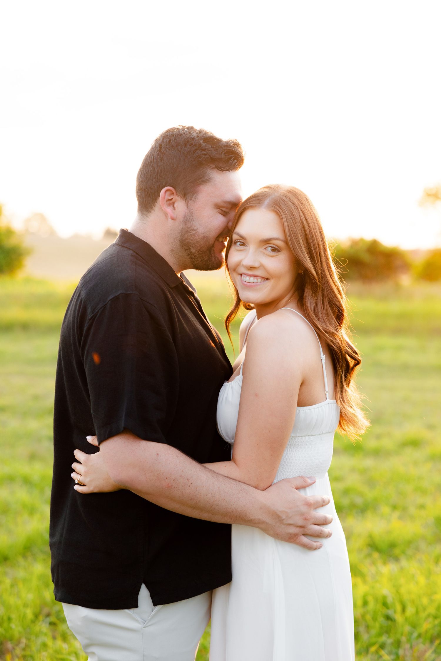 Candid moment between couple during golden hour photoshoot in countryside setting.