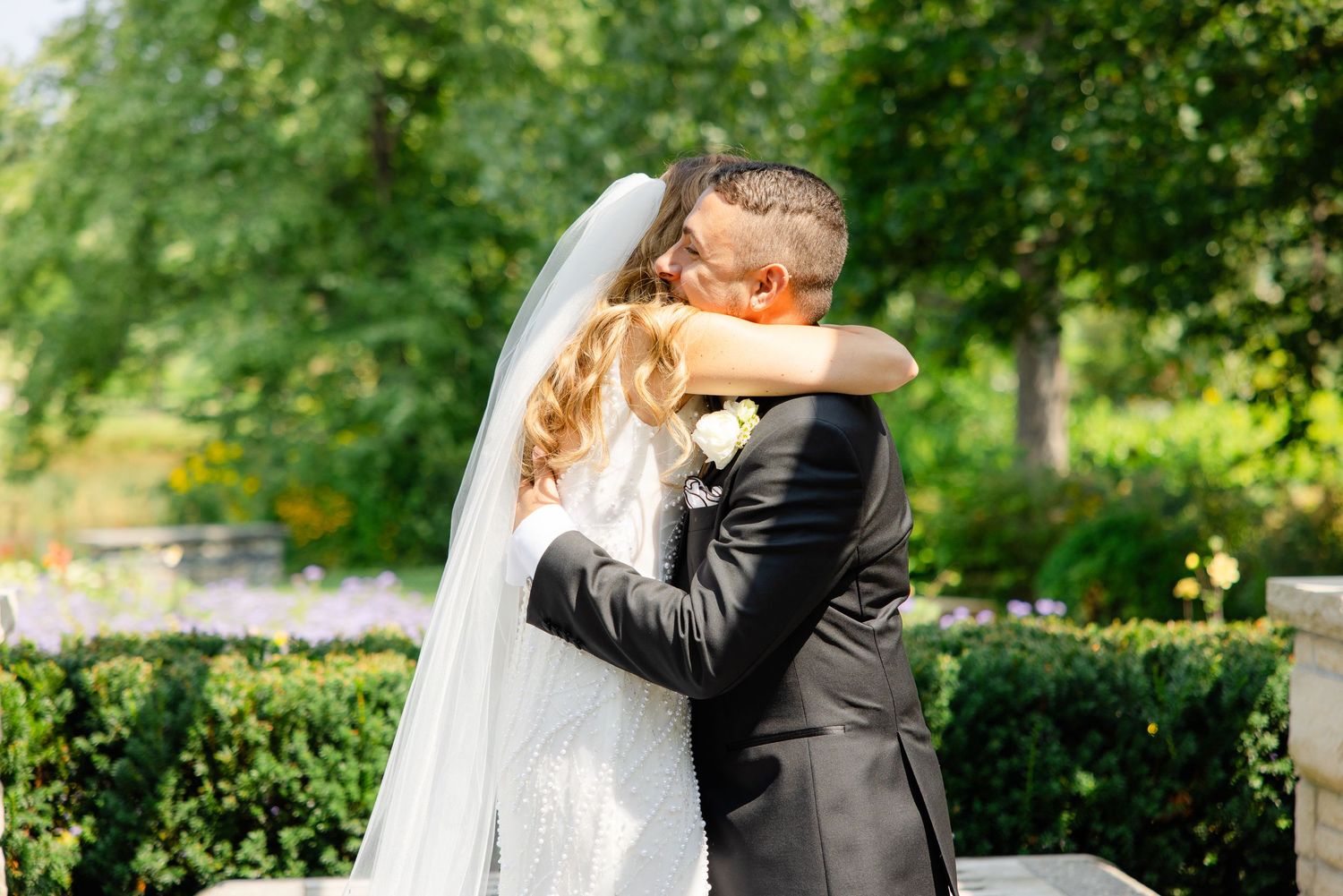 A tender embrace between newlyweds in a sunlit garden setting.