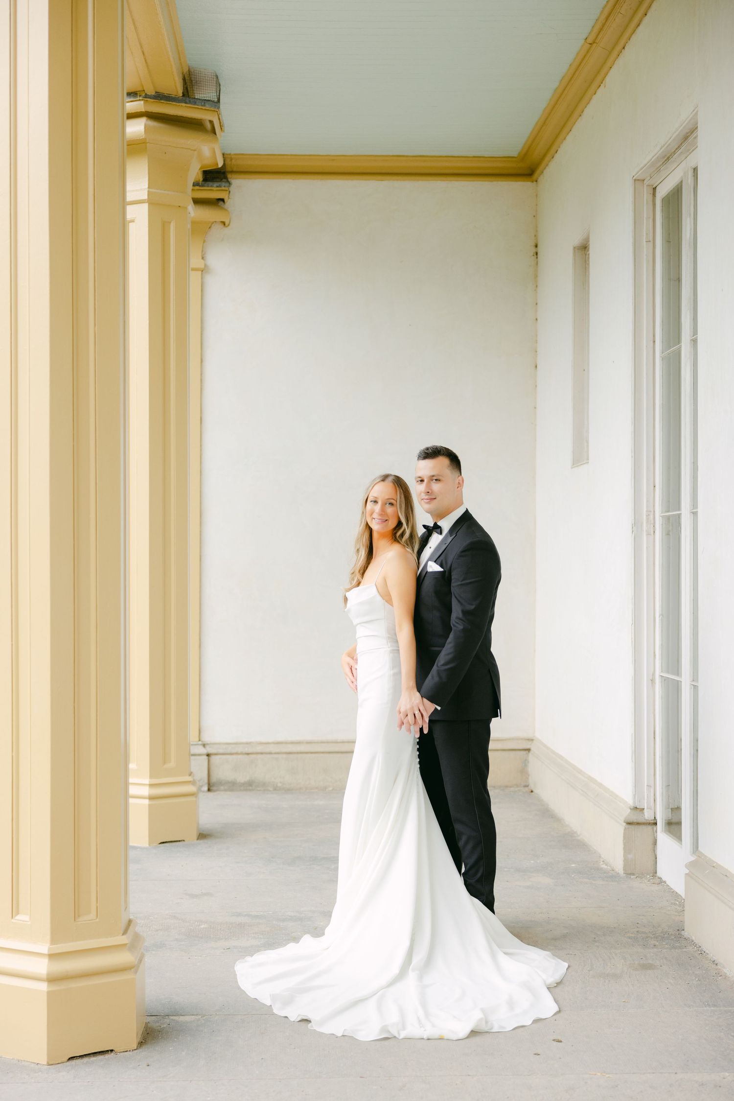 Full-length wedding portrait of couple in elegant colonnade with flowing white gown.