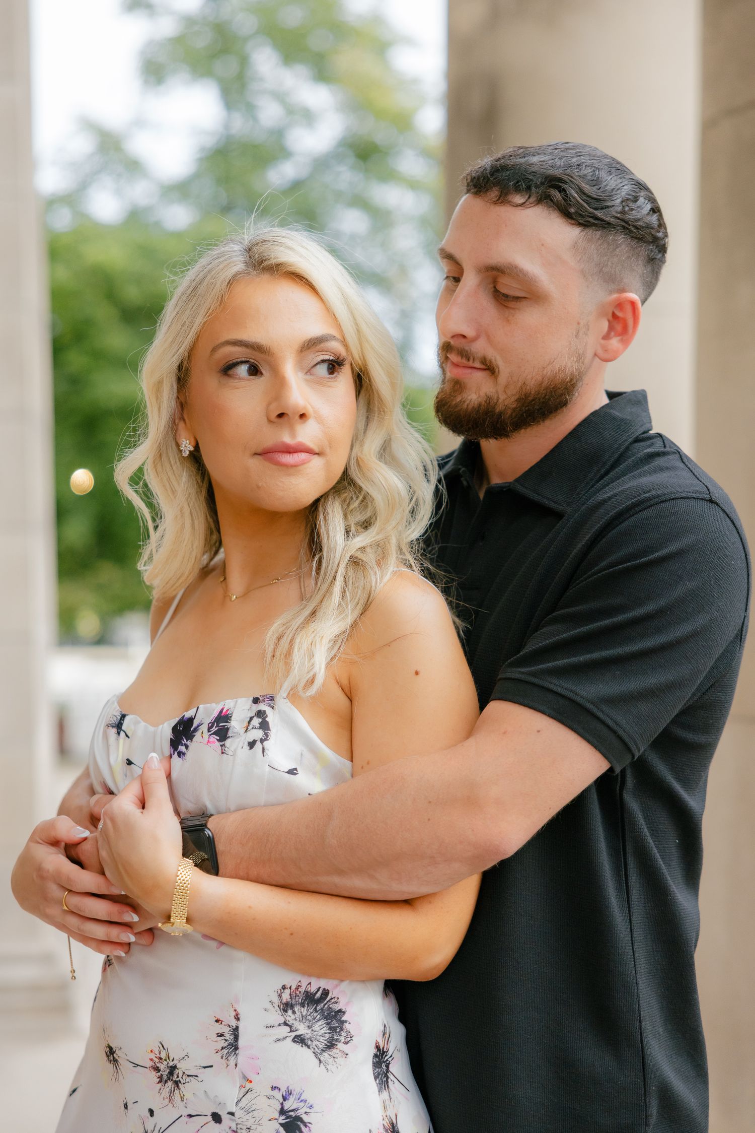 Stylish couple in complementary outfits share an intimate embrace between stone pillars.