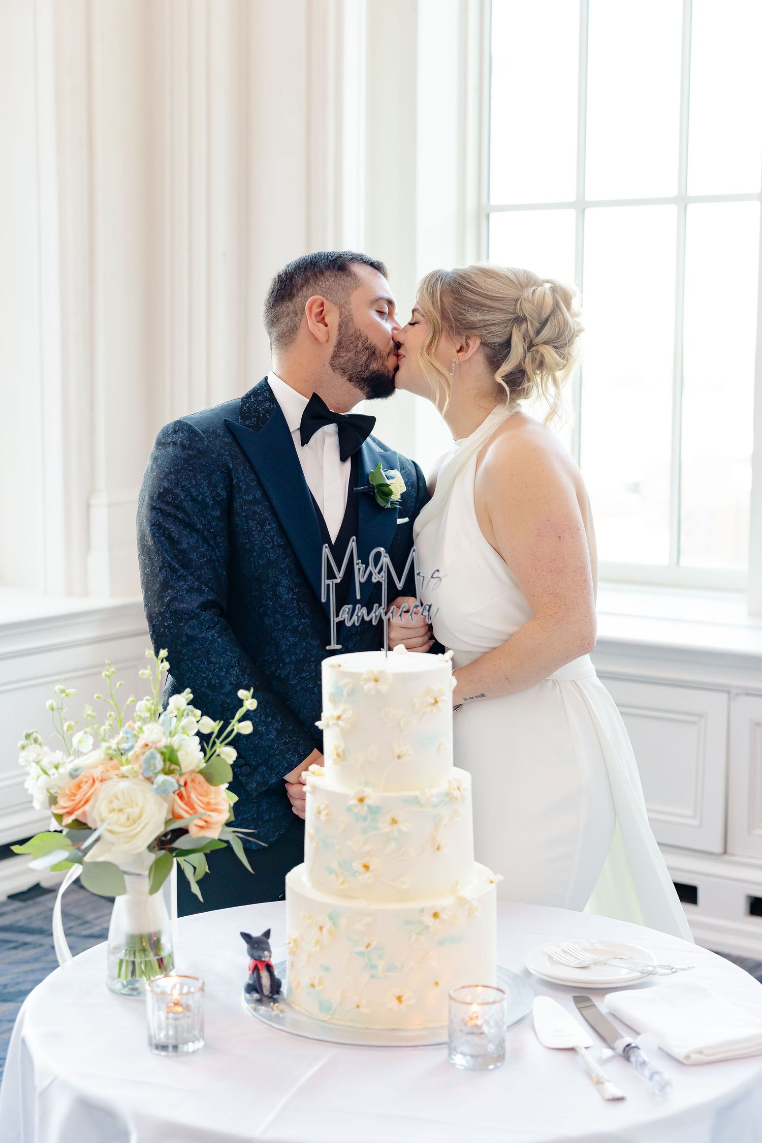 Wedding cake table setting with floral arrangements and elegant white tiered cake.