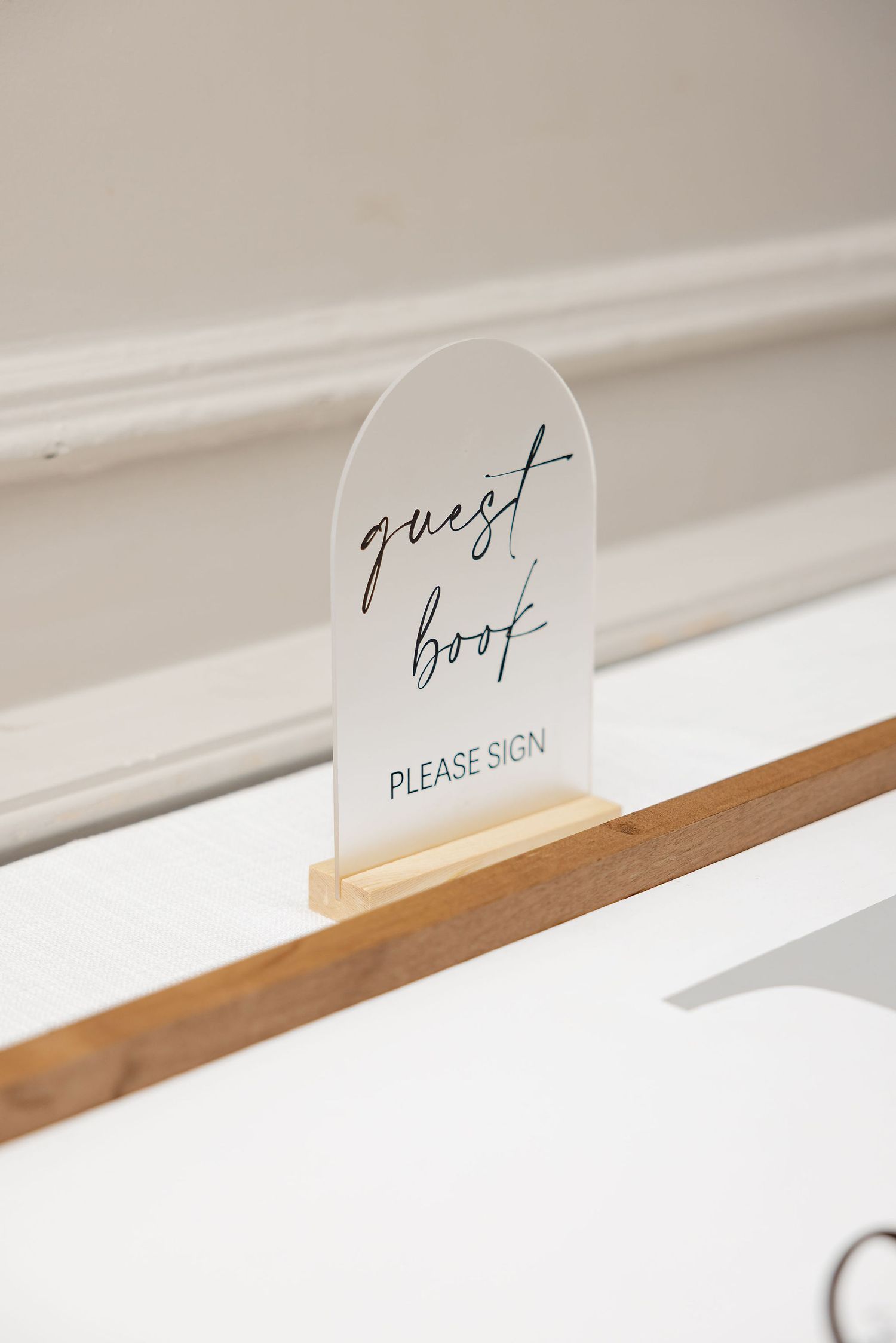 Minimalist guest book sign displayed on wooden ledge with clean typography.