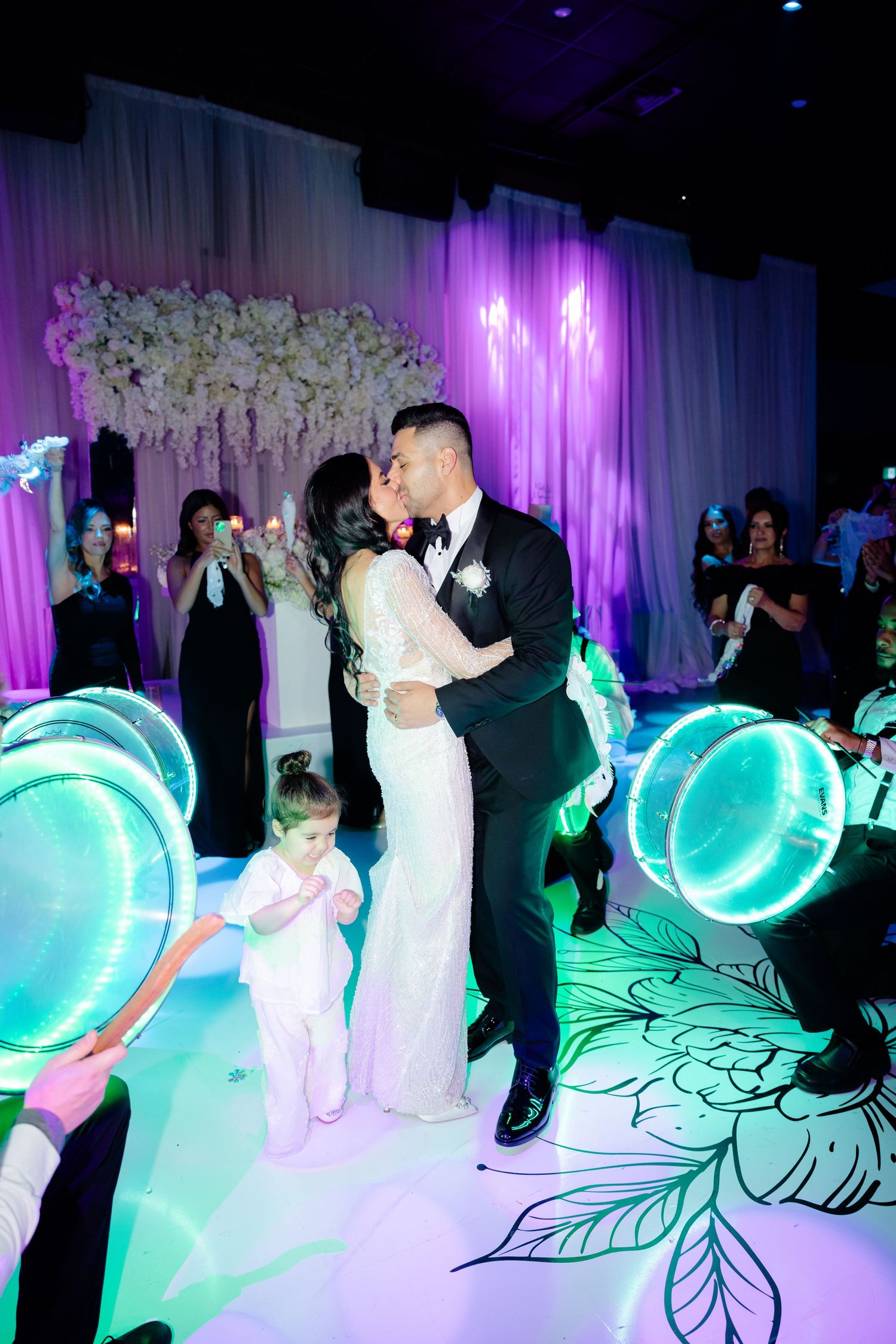 Couple sharing dance moment surrounded by glowing LED drums and turquoise lighting effects.