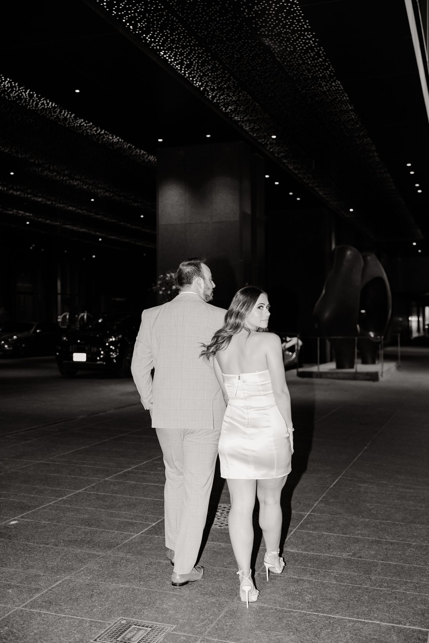 A romantic black and white photo of a couple walking together in formal attire.