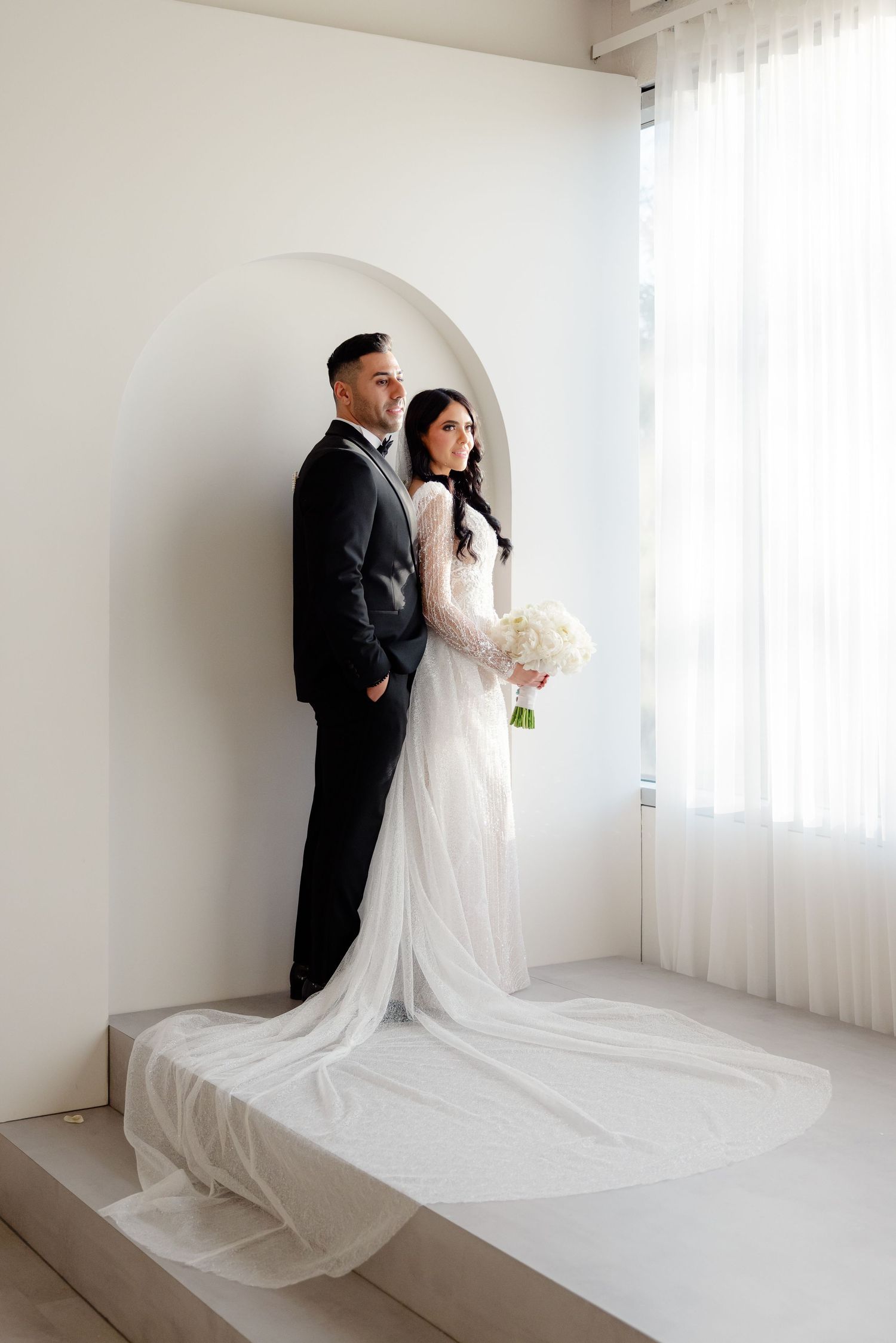 Classic wedding portrait of couple standing on raised platform in minimalist white setting.