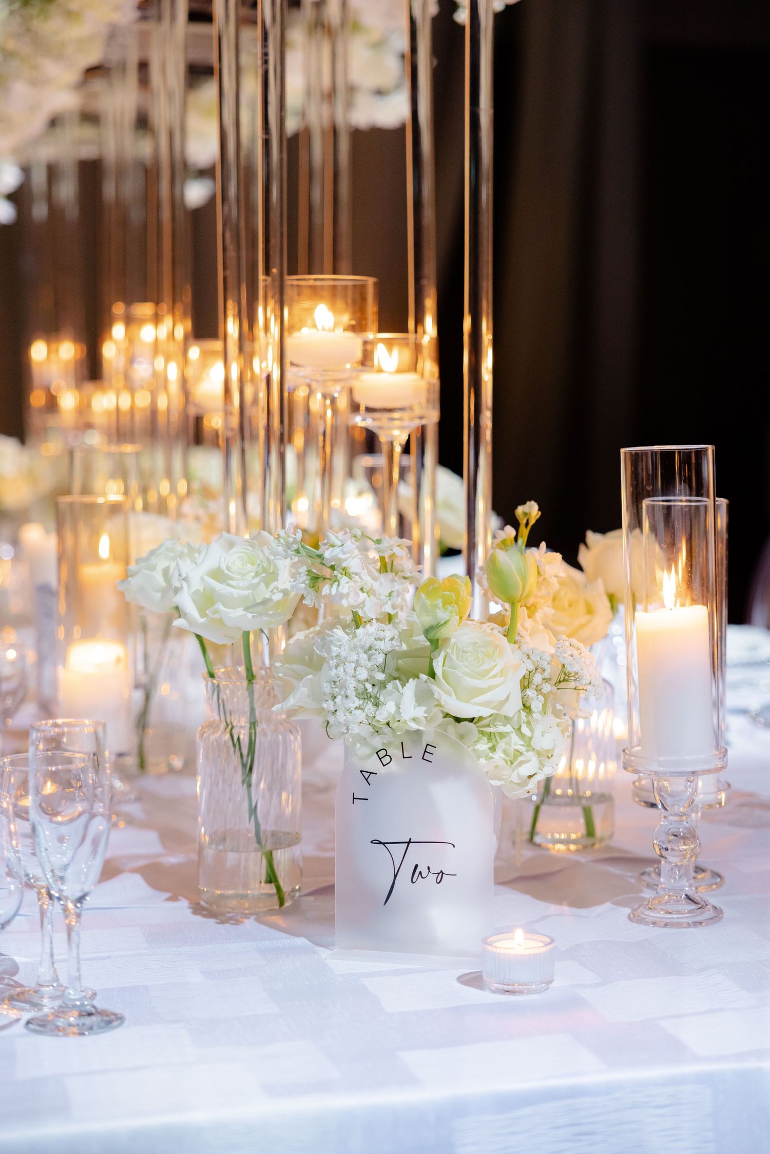 Romantic table setting with white roses, tall glass candle holders, and elegant place cards.