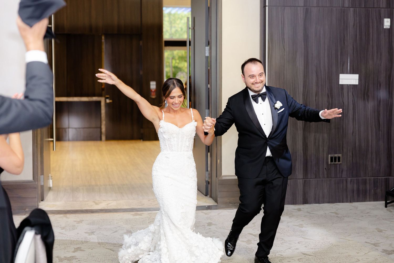 A joyful couple in wedding attire celebrate with arms raised as they exit a building together.