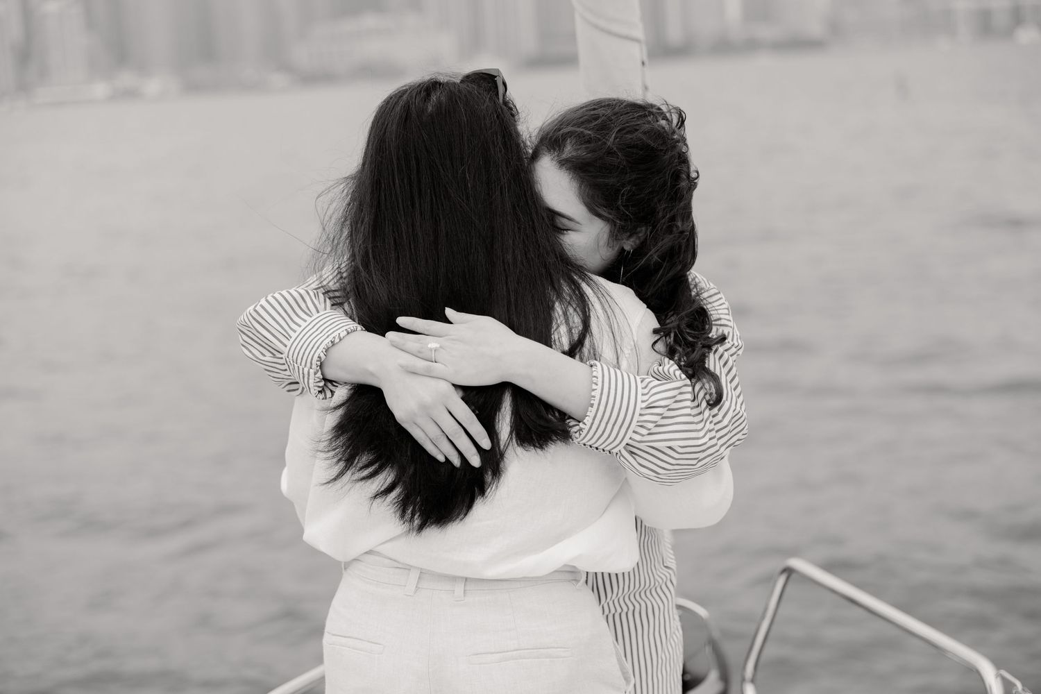Two women share a warm embrace while wearing white and striped clothing in a black and white photograph.
