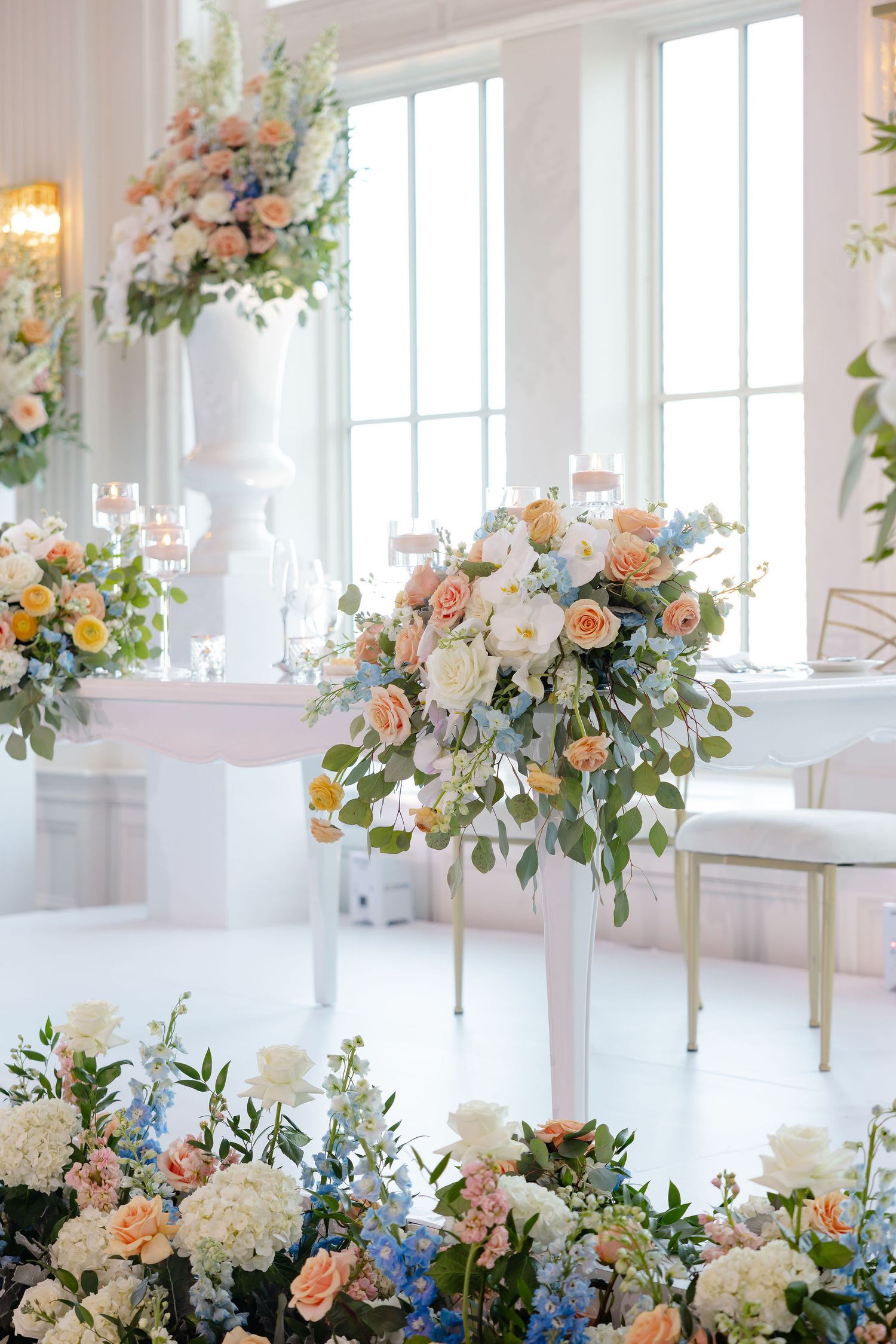 Romantic wedding reception space with peach and blue floral centerpieces and tall windows letting in natural light.