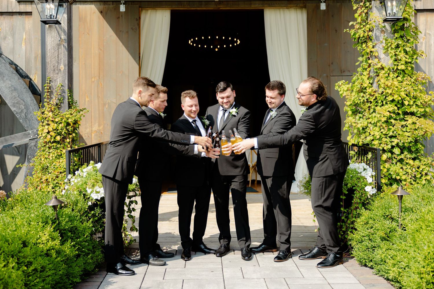 Groomsmen join hands in a circle for a celebratory moment outside a rustic barn venue.