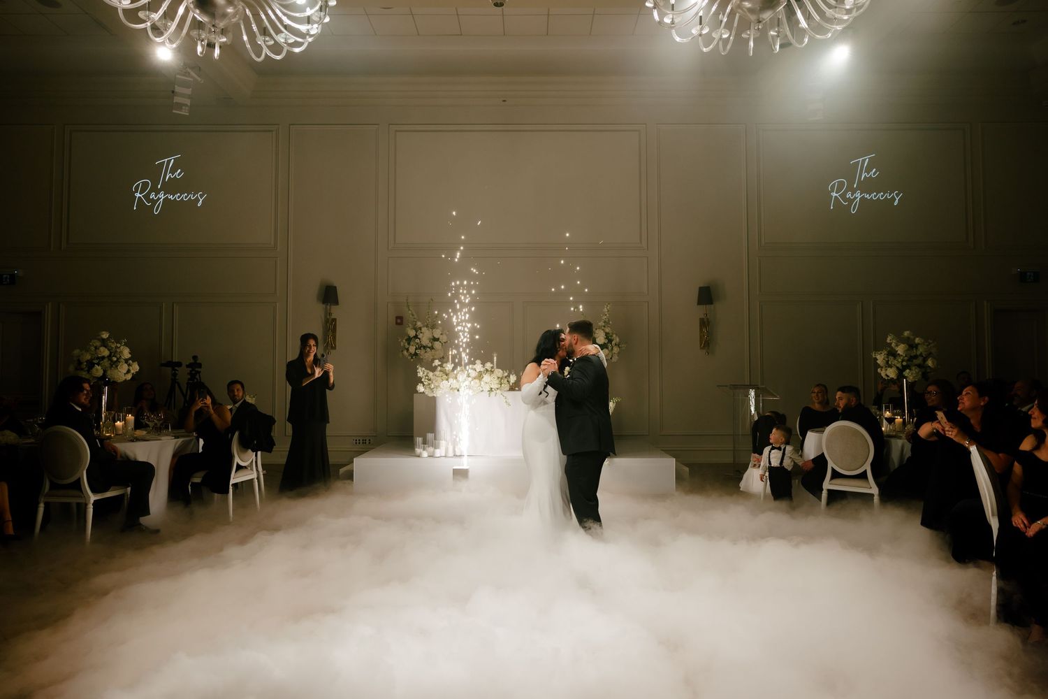 Wedding couple dances surrounded by guests as fog rolls across their elegant ballroom venue.
