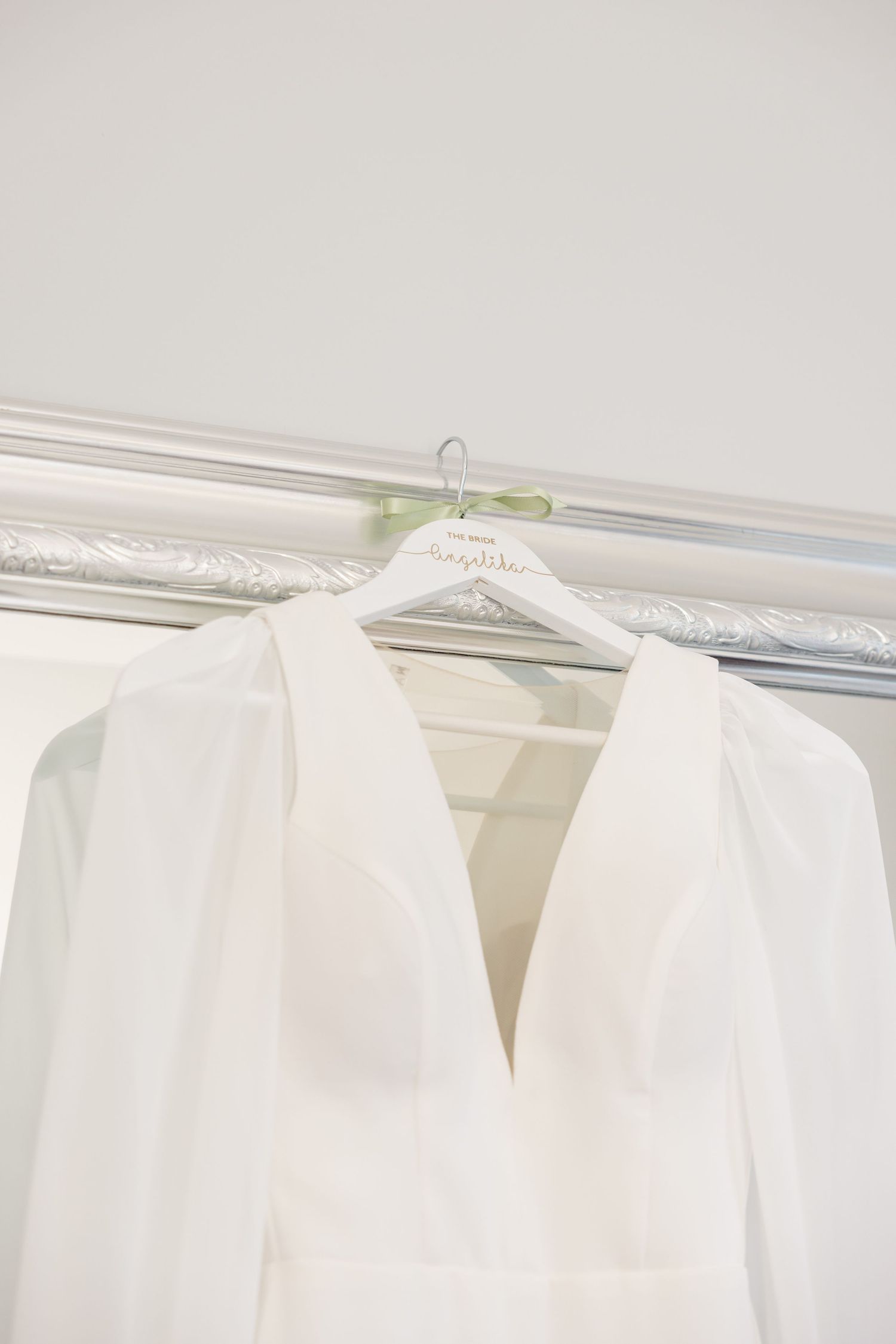 Elegant white wedding dress hanging on custom hanger against light background.