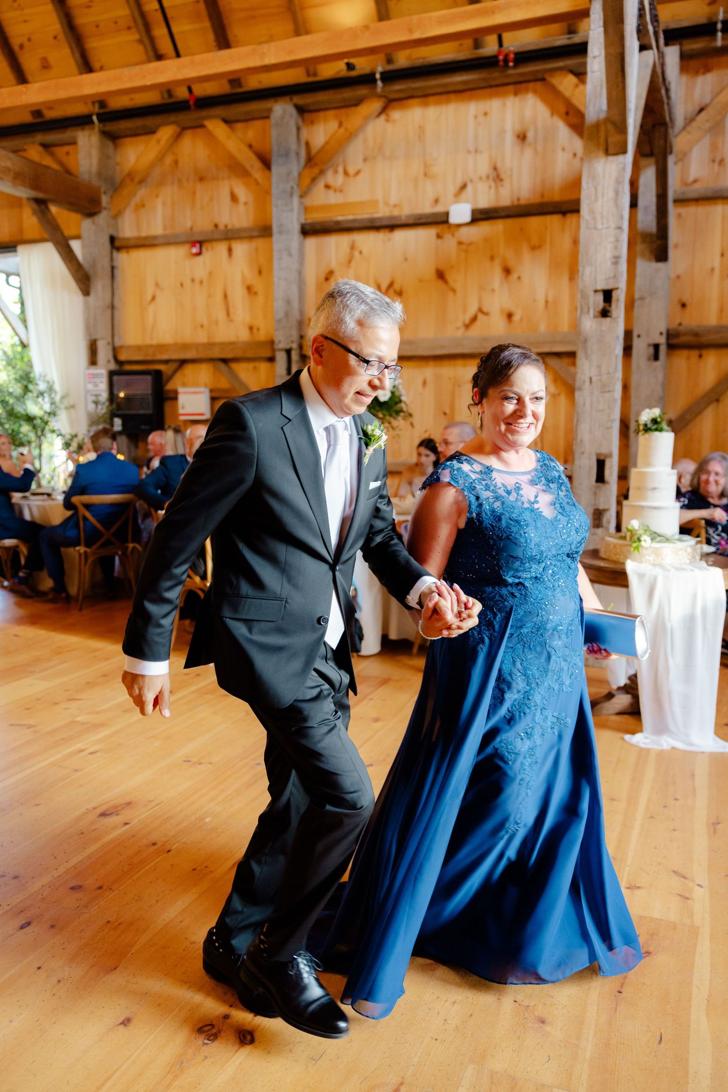A couple dances joyfully together in an elegant barn venue with wood beams and floors.
