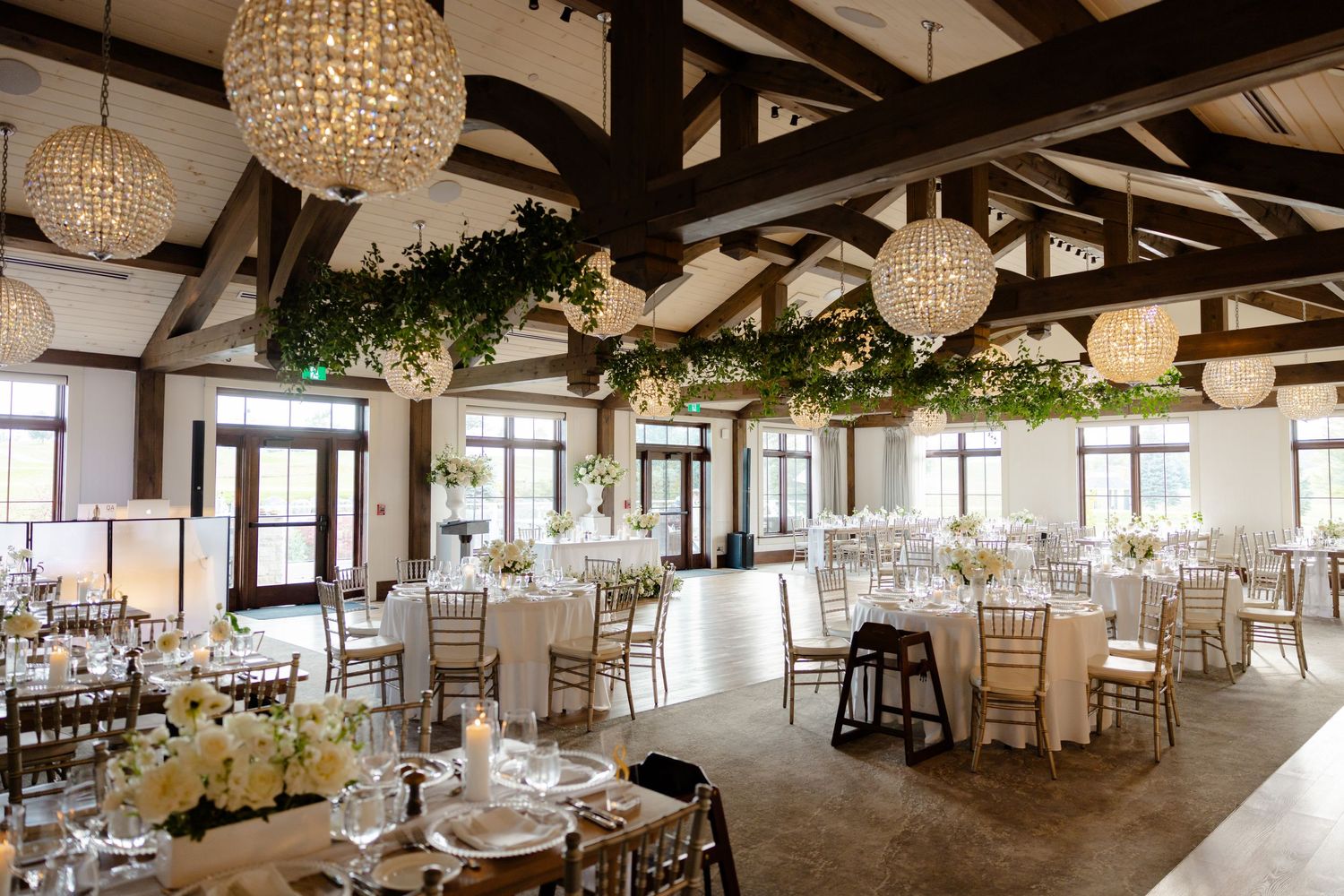 Elegant reception hall with crystal chandeliers, exposed beams, and round tables set for dining.