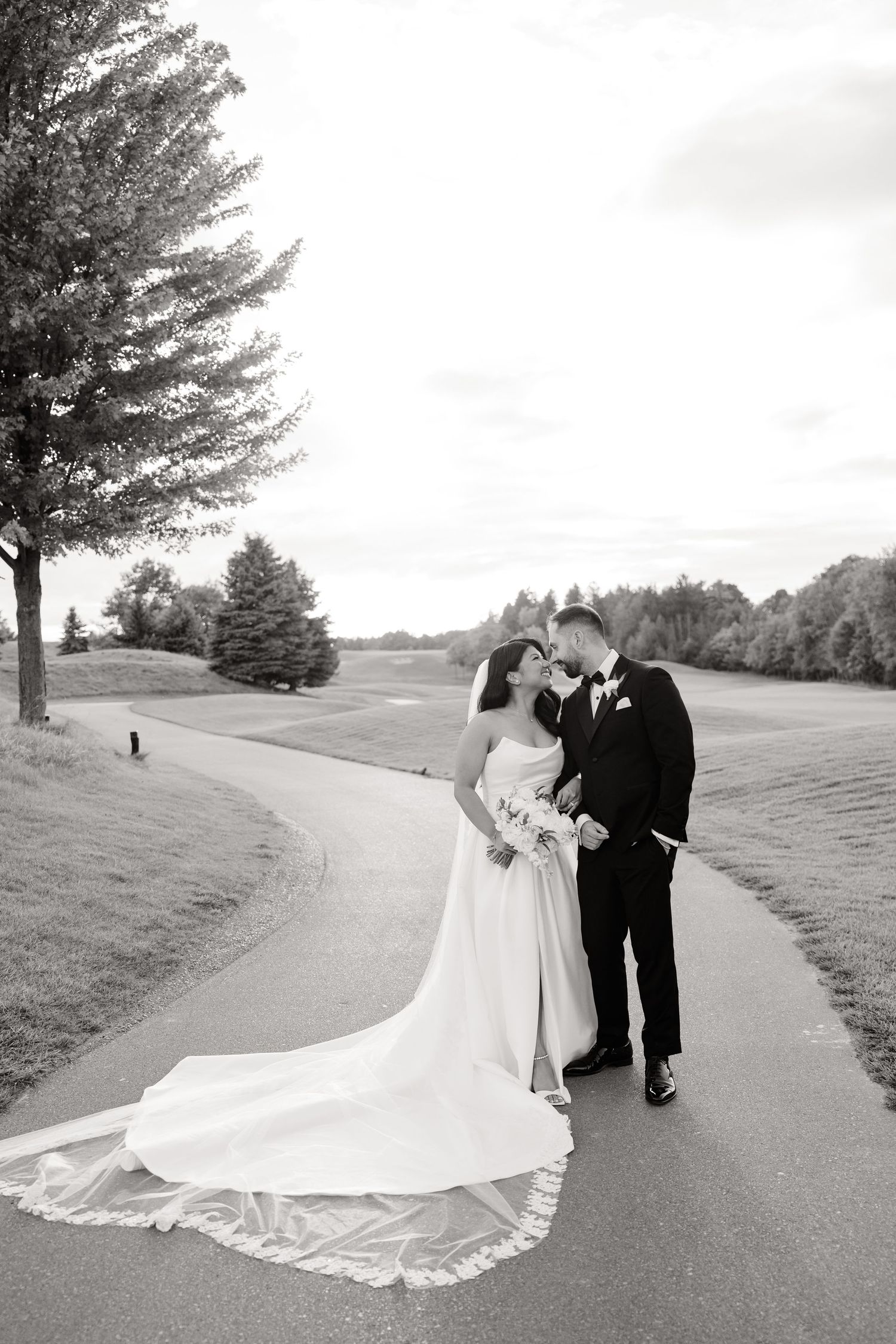 A black and white wedding photo of a couple sharing an intimate moment on a winding golf cart path.
