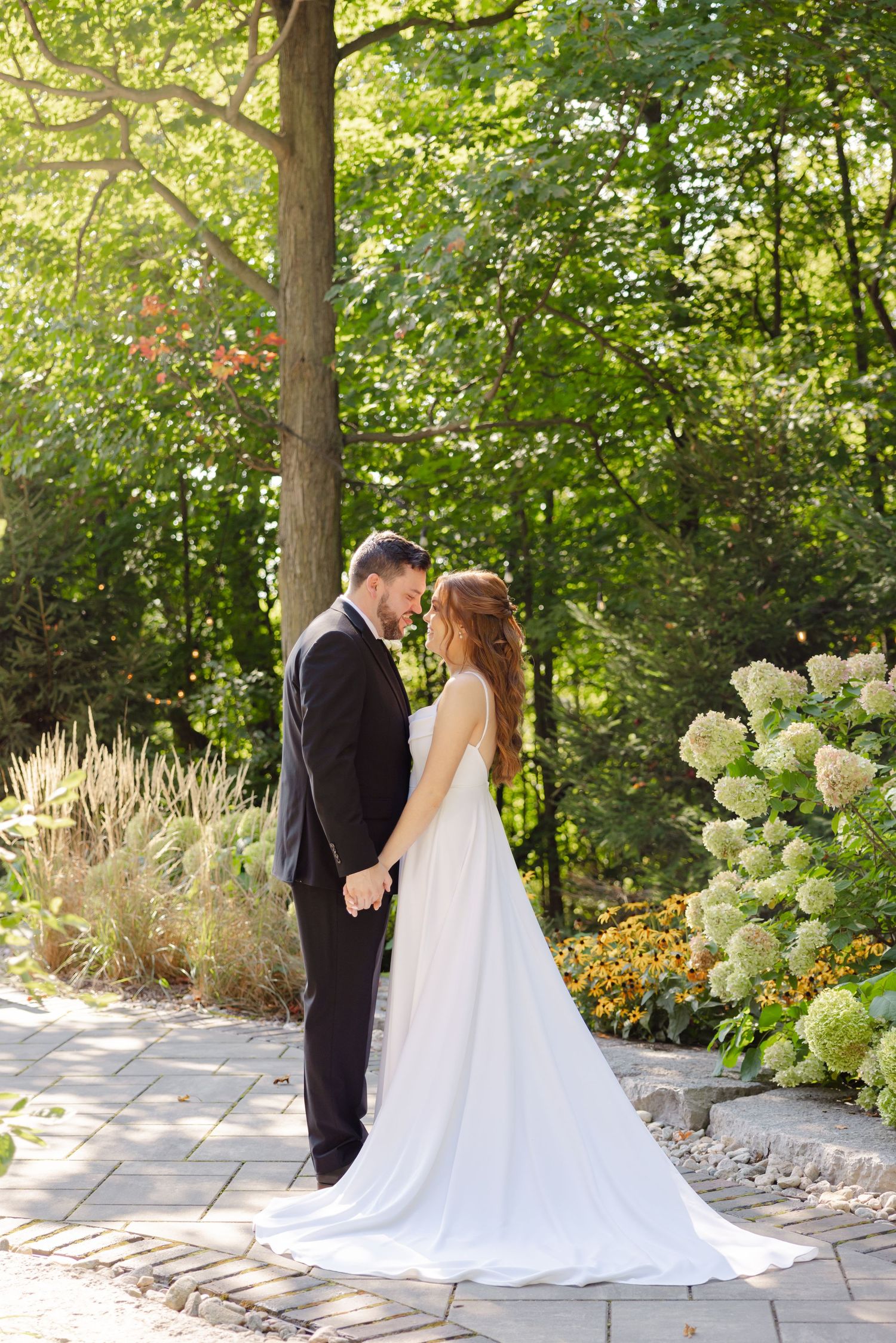 An intimate wedding portrait in a garden setting with blooming hydrangeas and dappled sunlight.