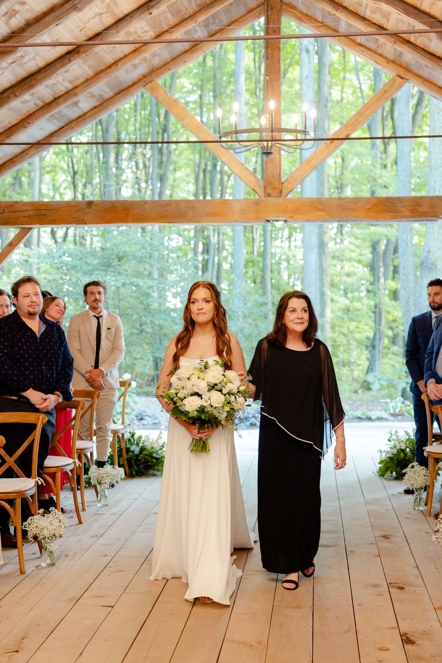 Wedding processional in a rustic wooden chapel with floor-to-ceiling windows overlooking a forest.