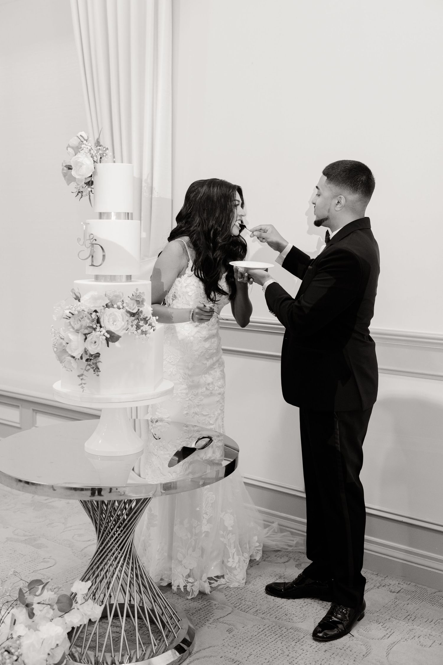 Black and white photo of a couple feeding each other wedding cake during their reception.