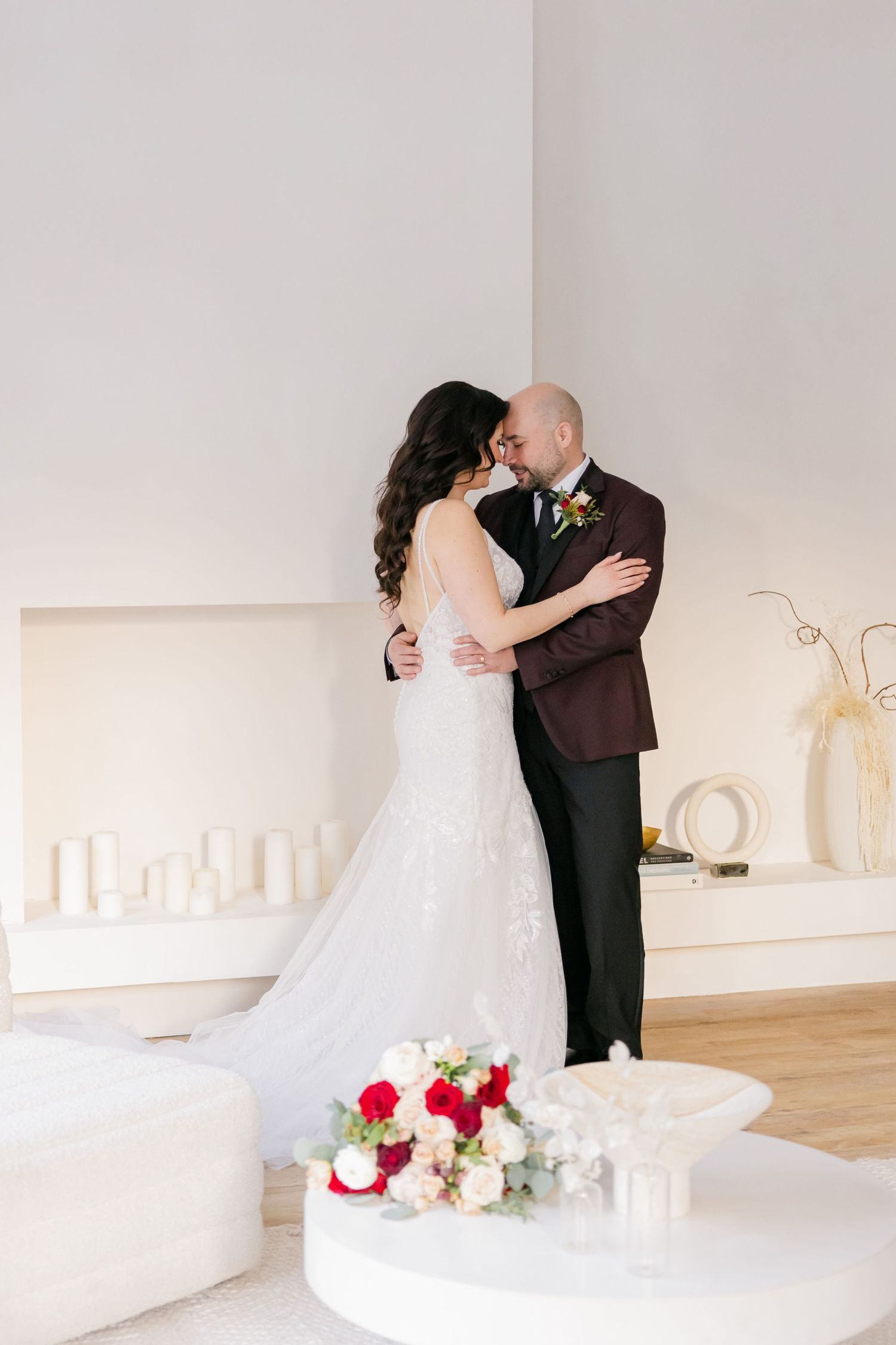 Romantic wedding kiss captured in a minimalist white room with floral arrangements.
