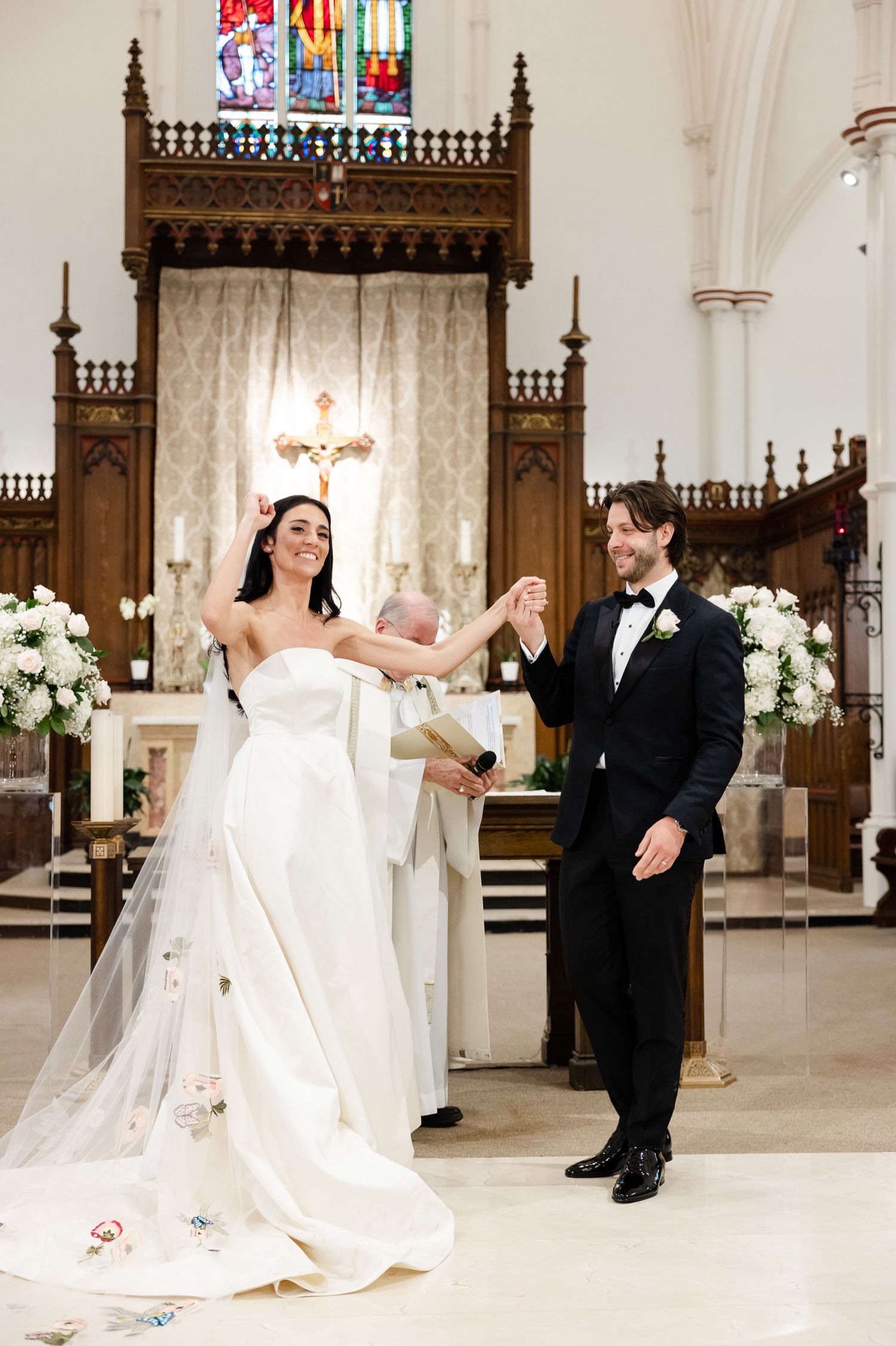 Joyous wedding celebration moment at church altar with ornate wooden details and stained glass backdrop.