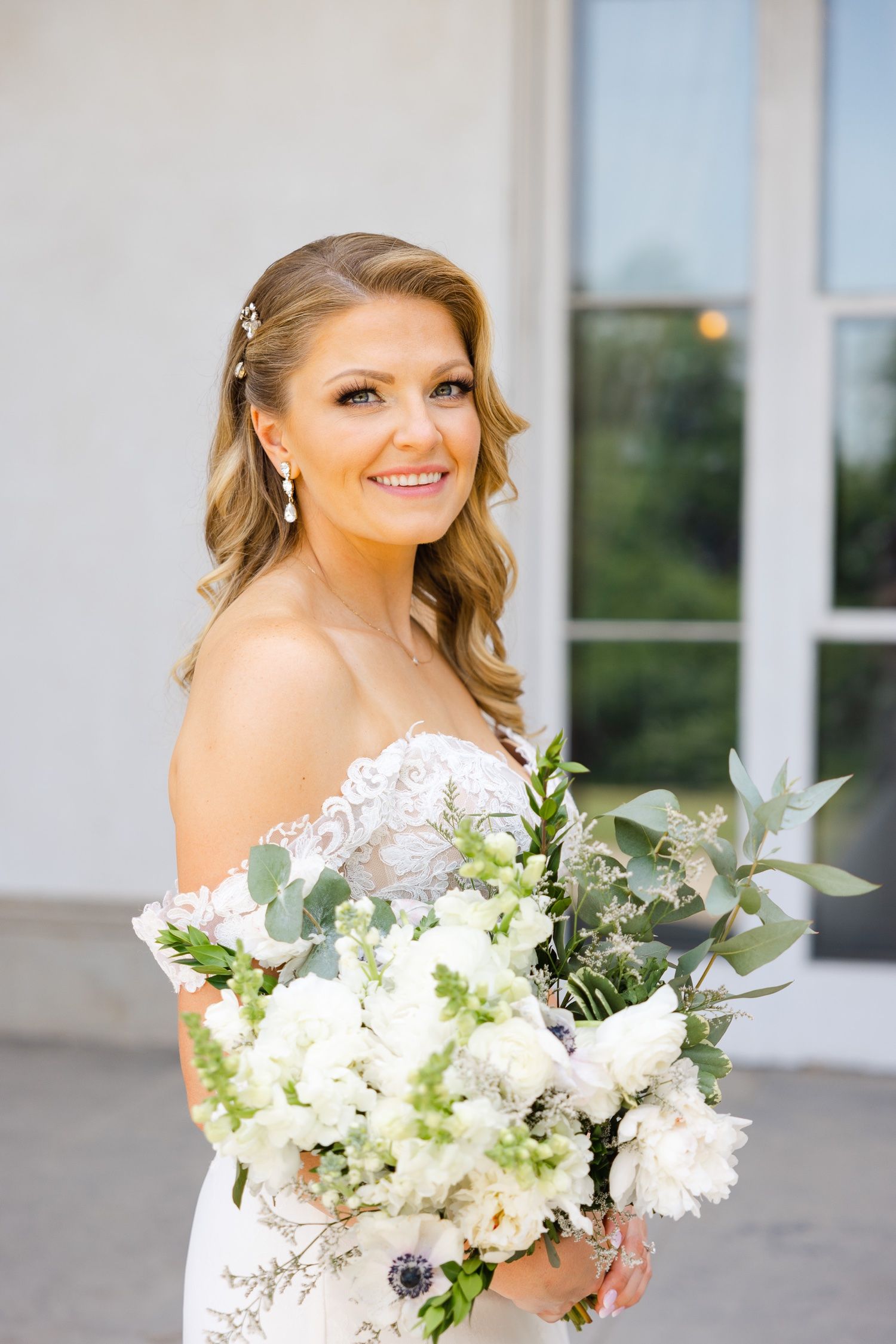 A romantic bridal portrait showcasing an off-shoulder lace gown and fresh white and green bouquet.