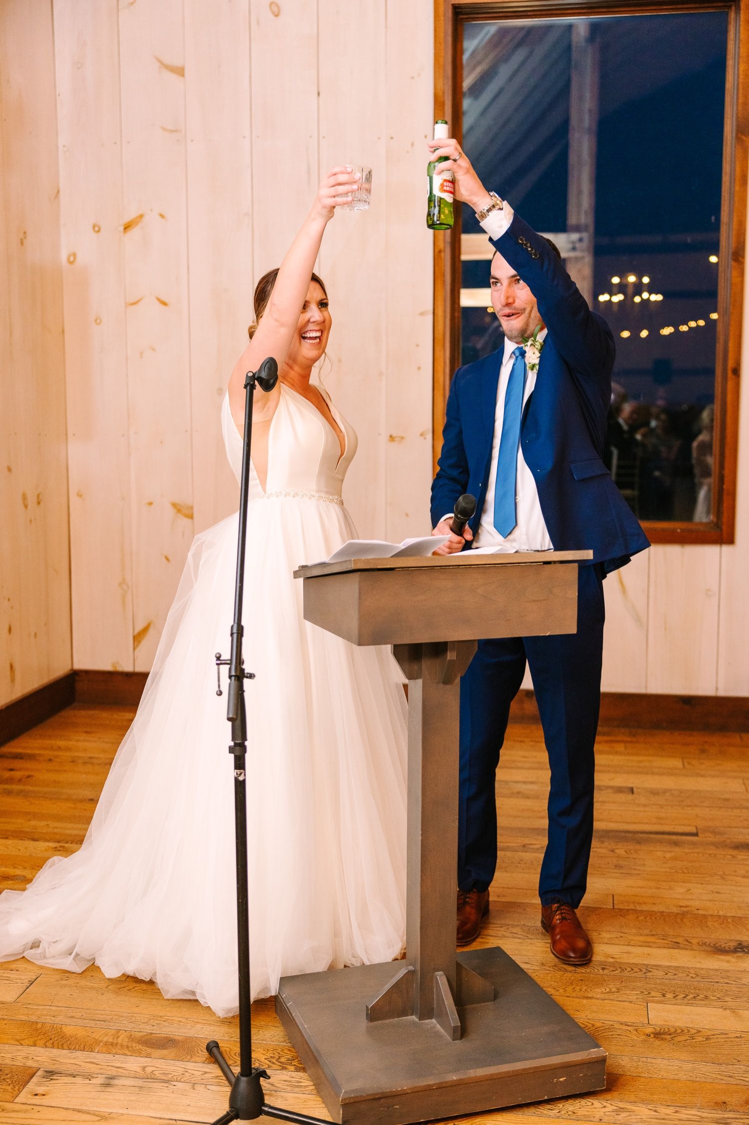 Newlyweds celebrate joyfully at wooden podium during wedding reception.